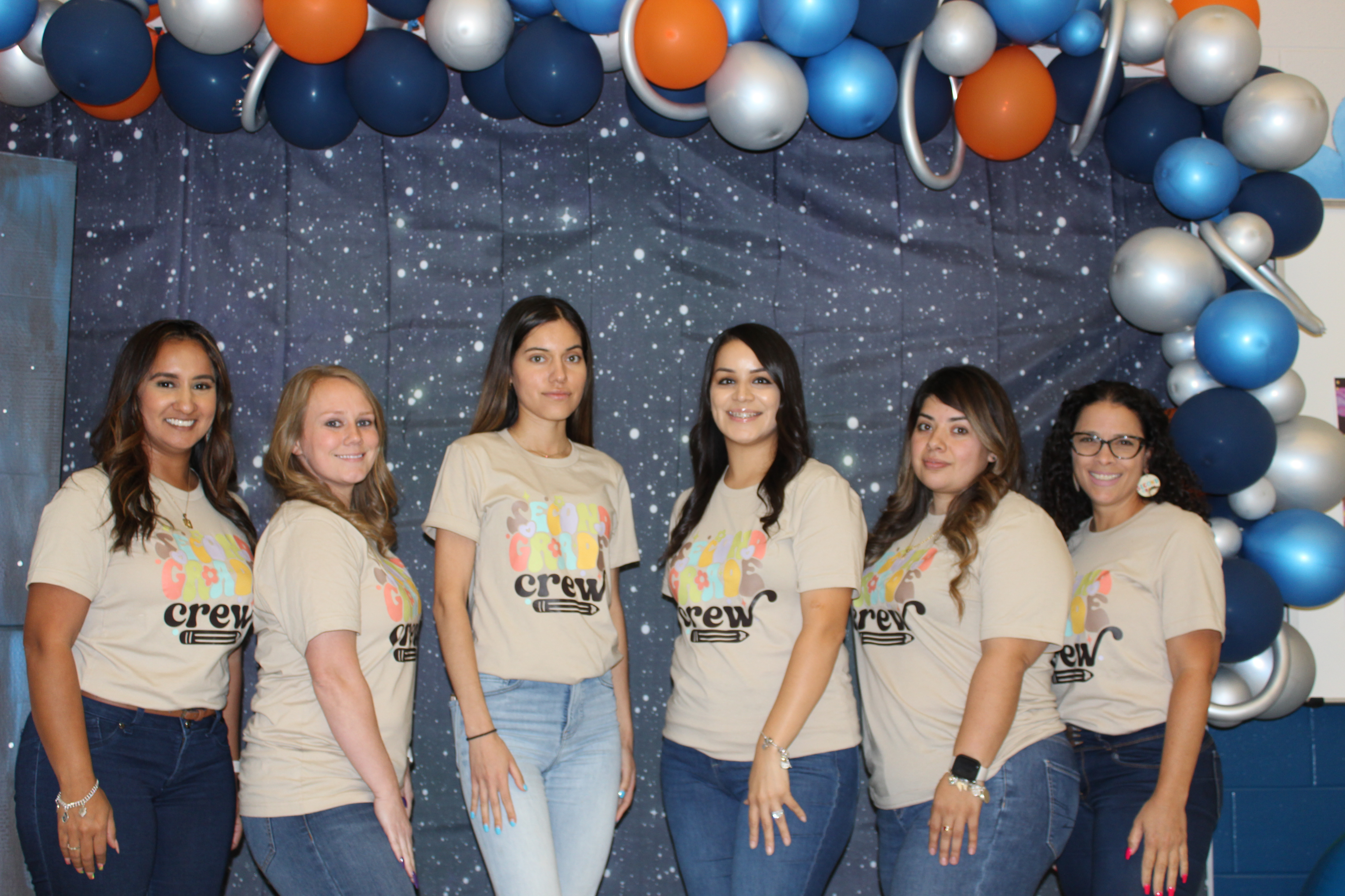 group of teachers standing posing in front of starry backdrop with tan shirts