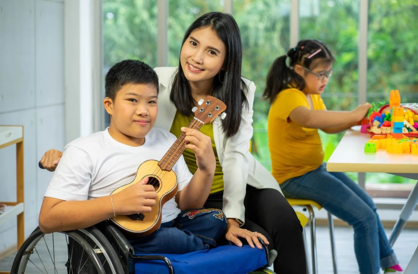 Image of boy with a disability playing the guitar on a wheelchair