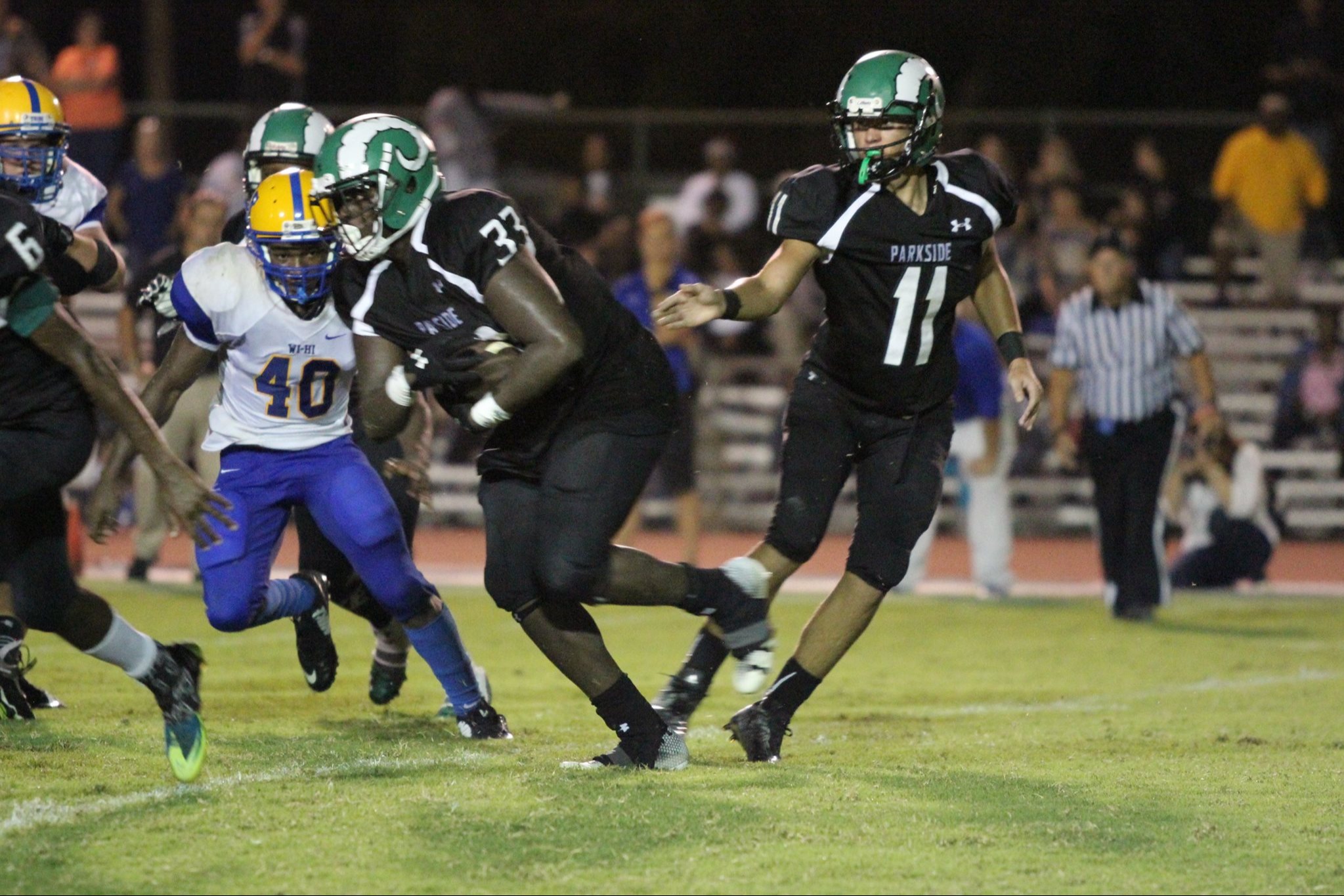 Image of high school football player running with the ball being approached by an opposing defender