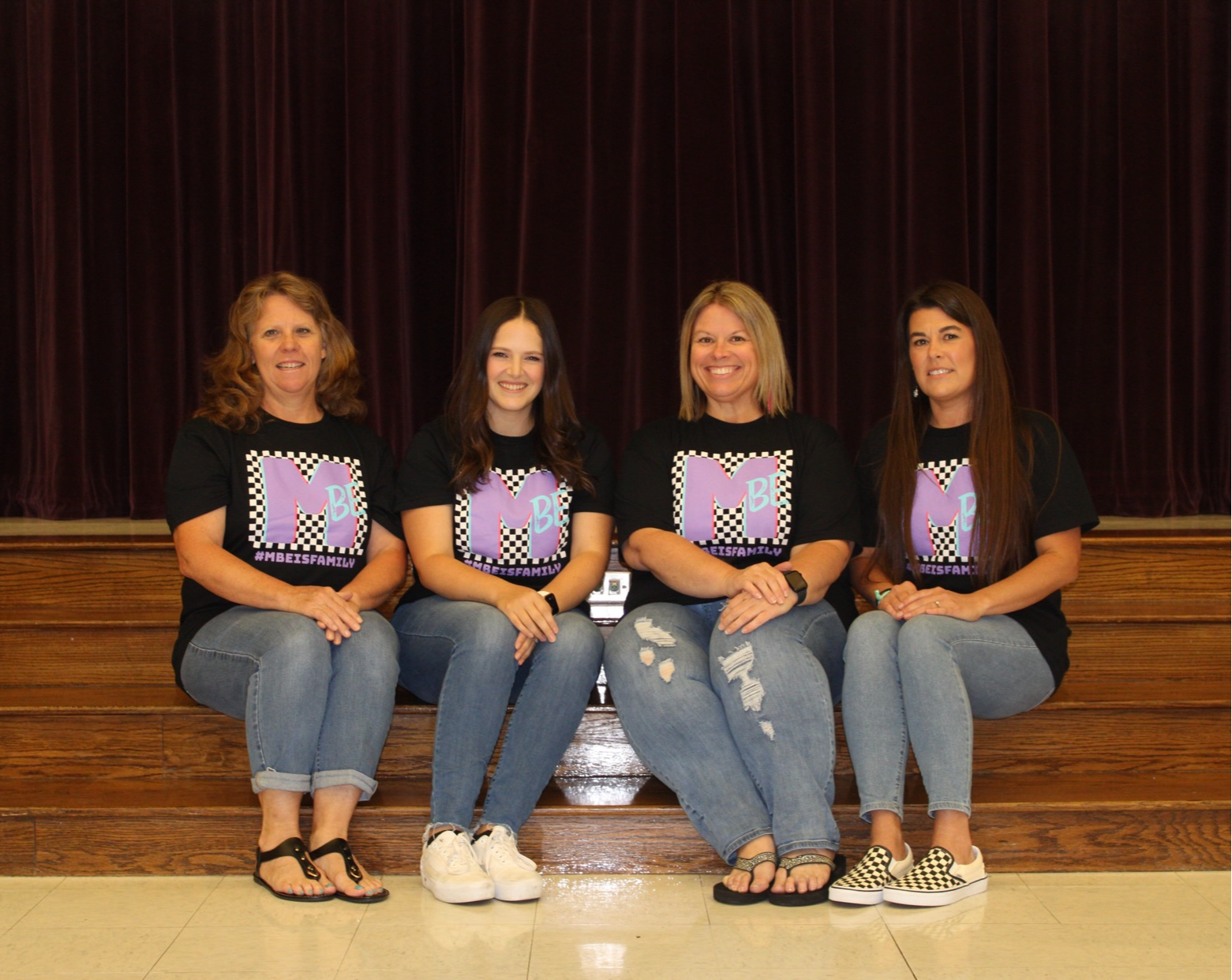 teachers in gray shirts posing in front of black backdrop with lights