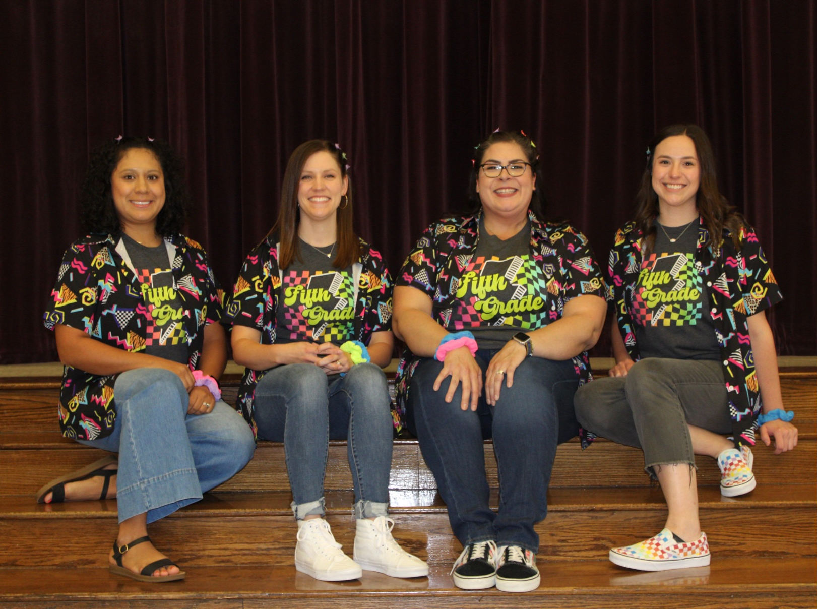 group of teachers in gray shirts posing near sofa inside school building