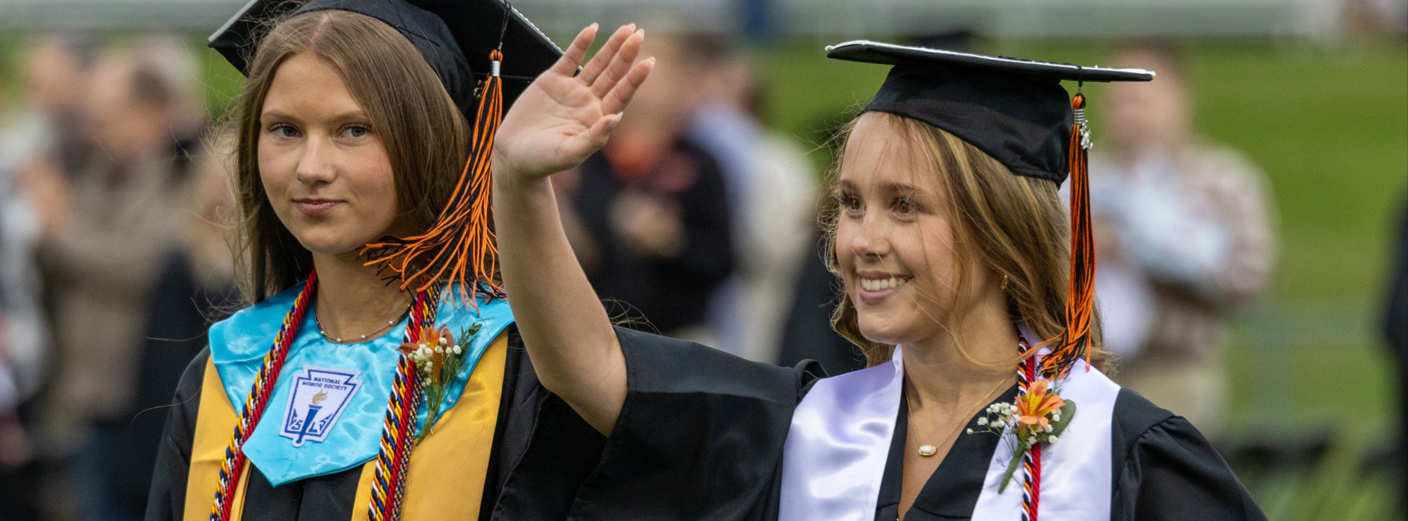 Students in graduation robes at a graduation ceremony. One is waving to the crowd