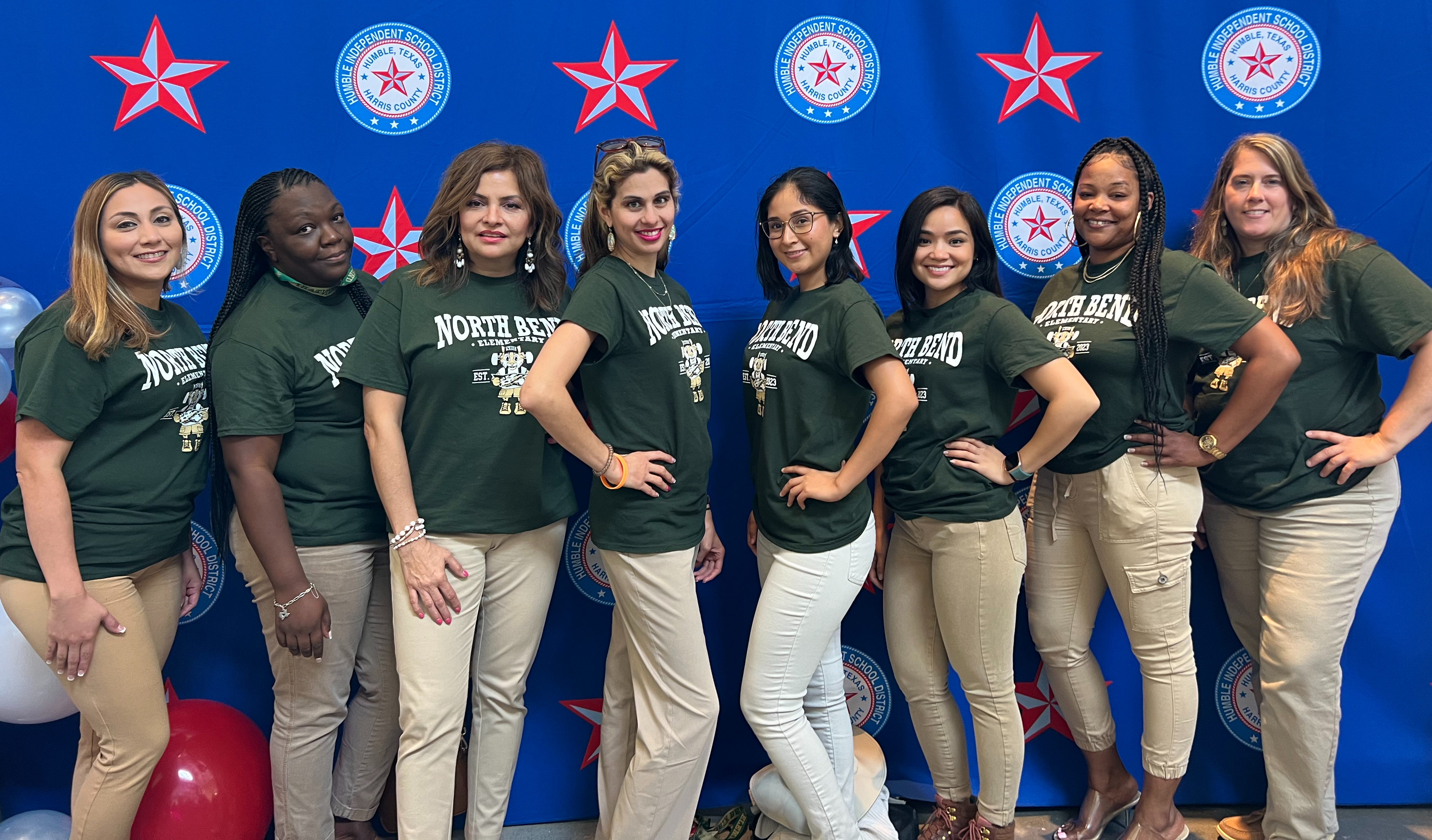 Second Grade teachers in green shirts standing posing in front of blue backdrop