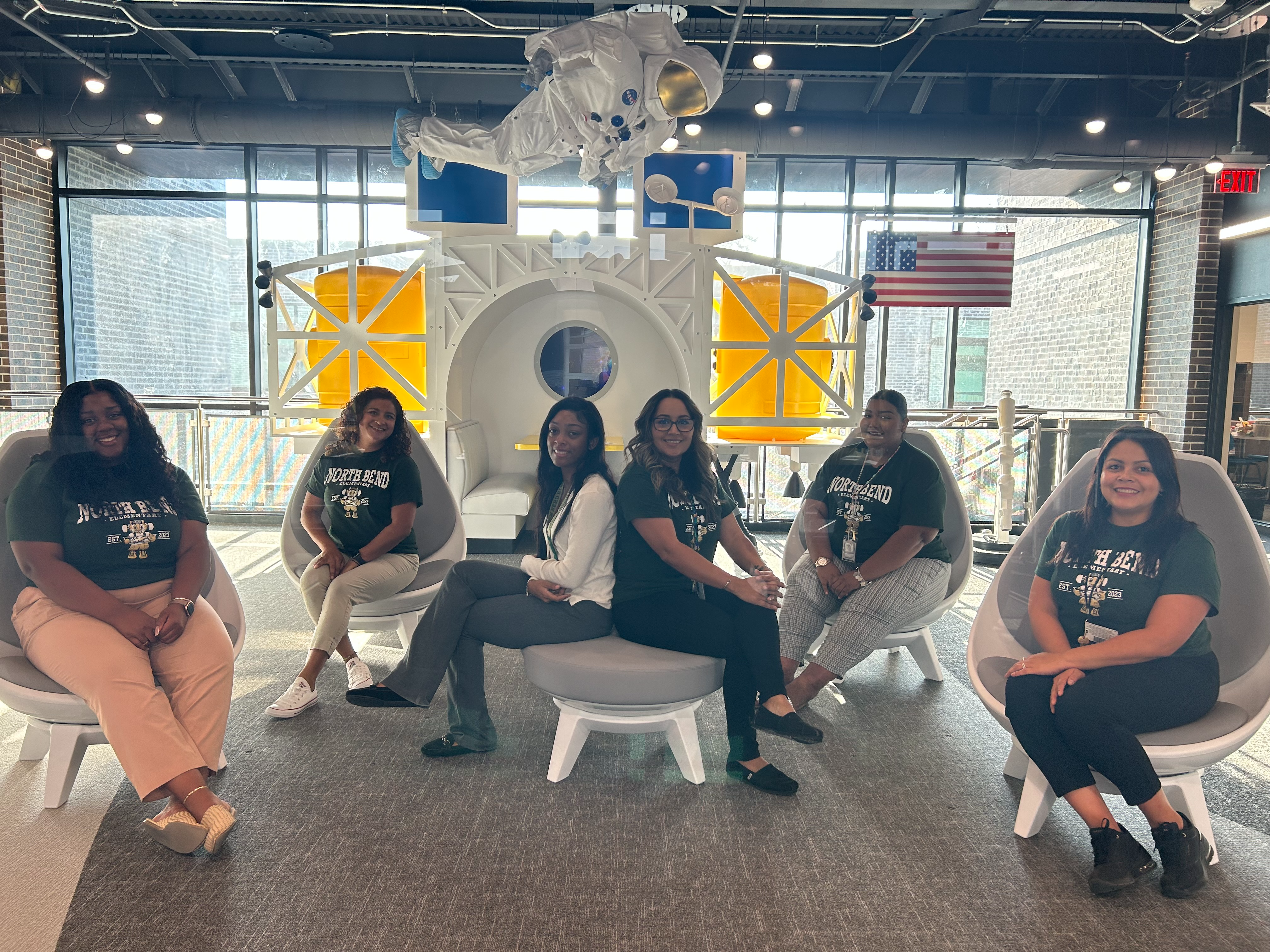 Fifth Grade teachers in green shirts posing sitting in chairs near spac props