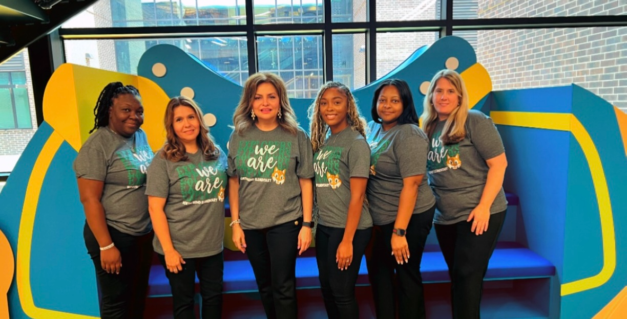 group of teachers in green shirts standing posing in front of humble isd logo backdrop