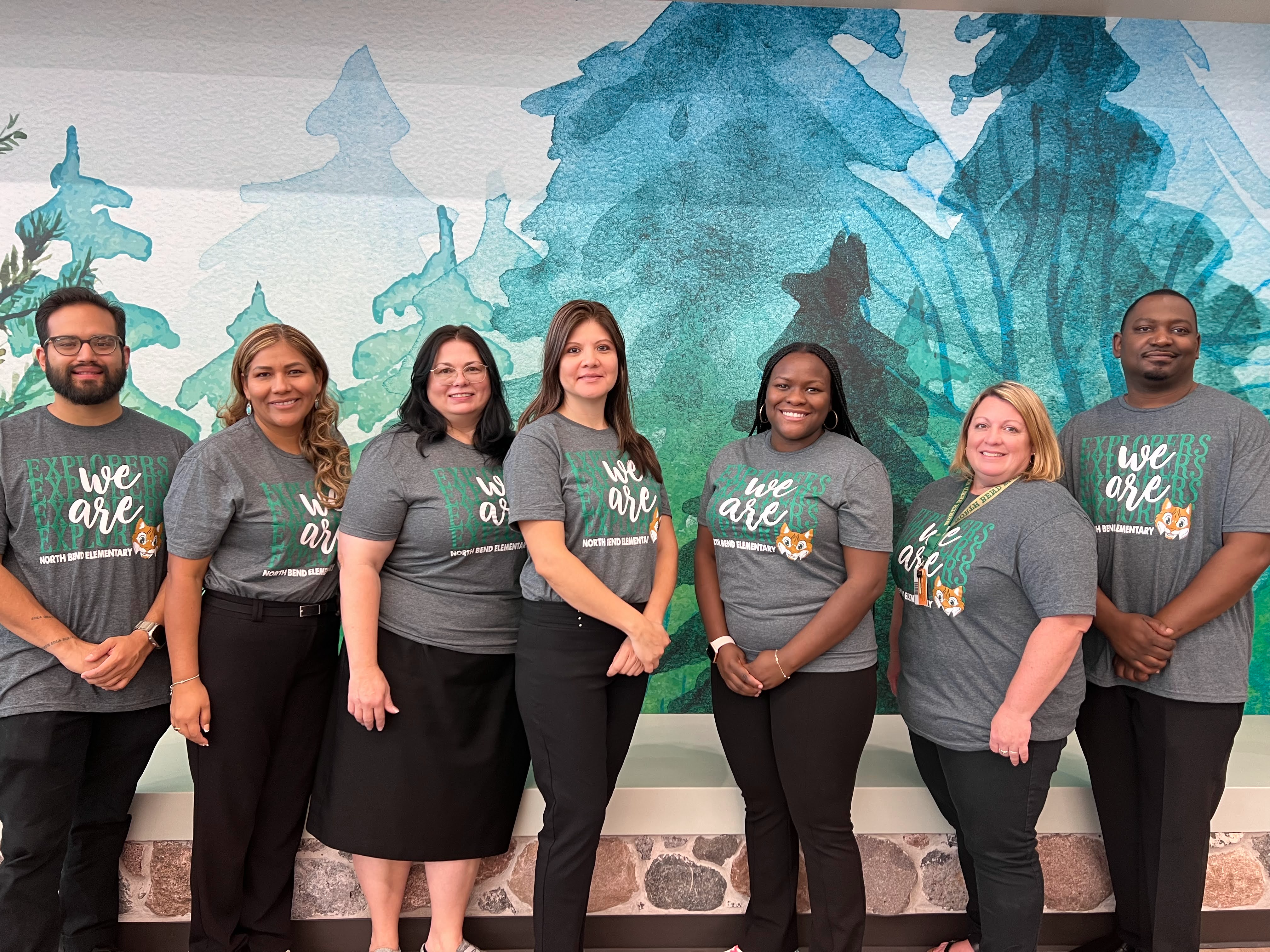 group of teachers in green shirts standing posing outside in front of building