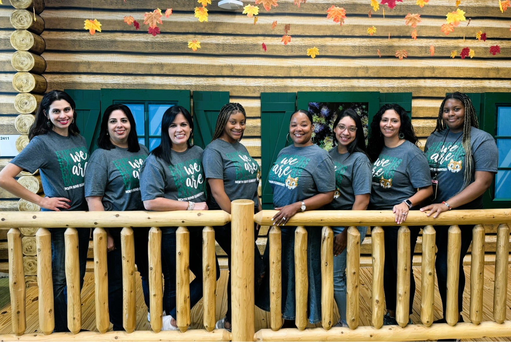 group of teachers in green shirts standing posing behind wooden fence structure inside school