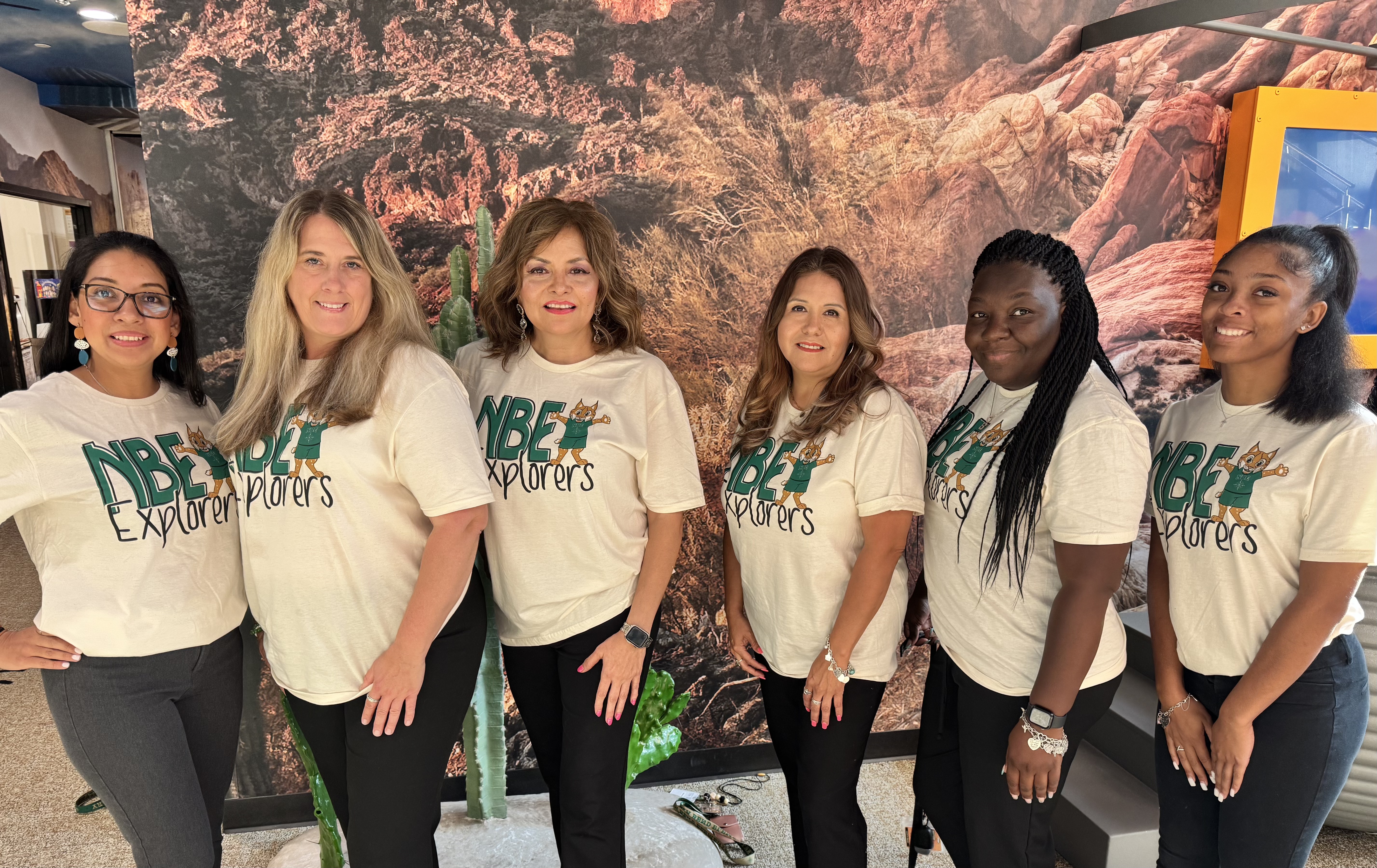 group of teachers in green shirts standing posing in front of humble isd logo backdrop