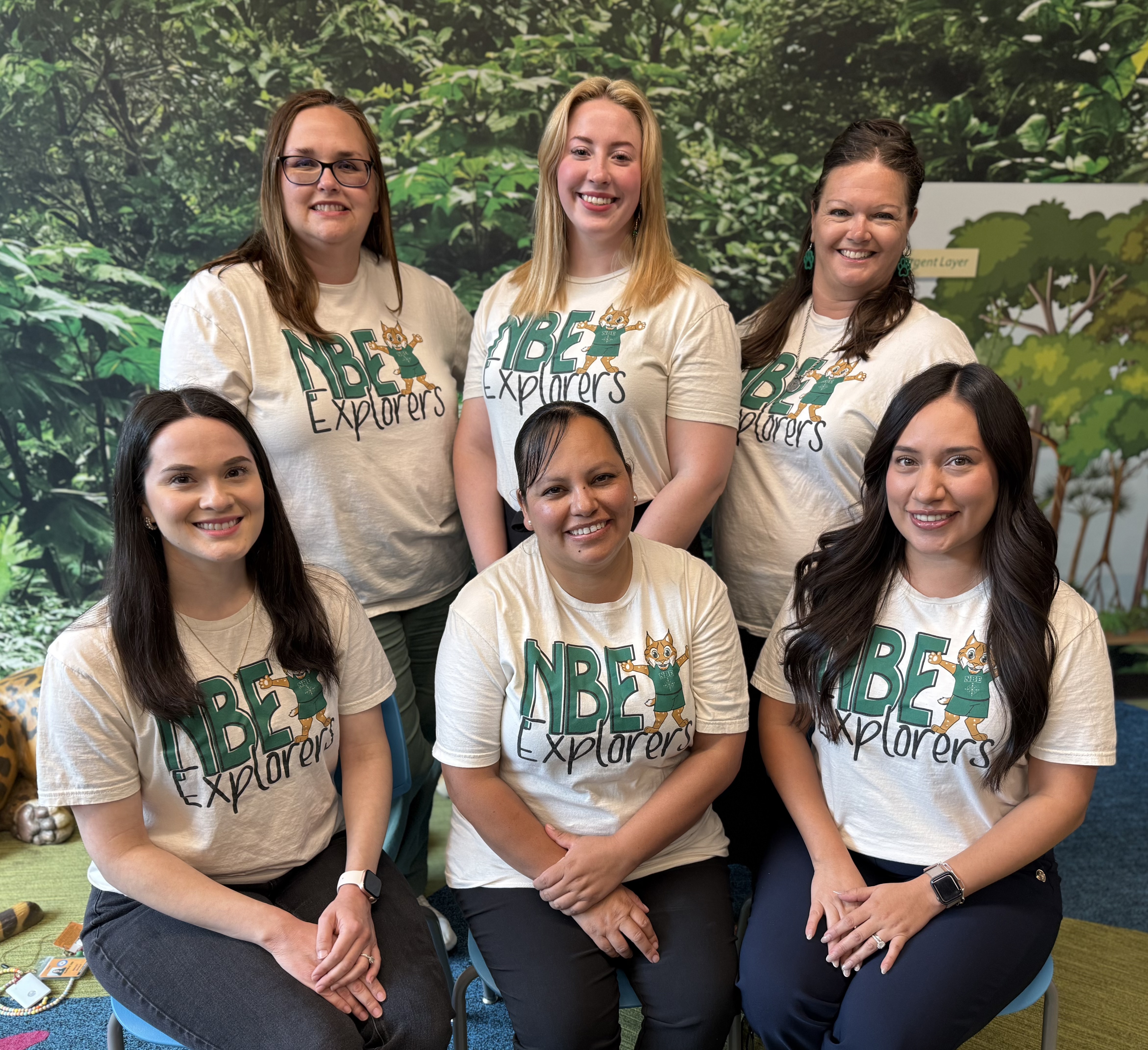 group of teachers in green shirts posing outside in front of greenery and building