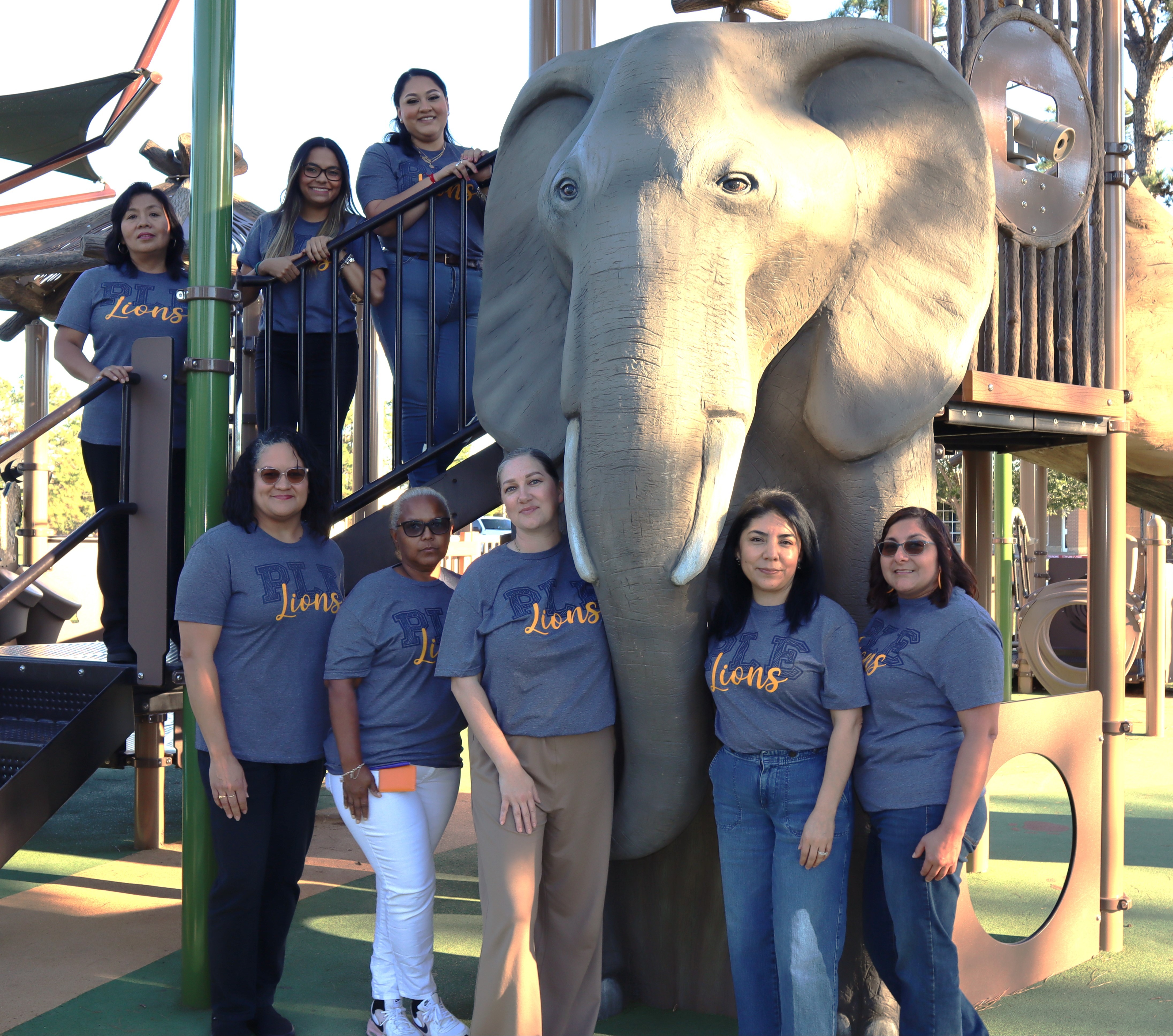 group of teachers posing near lion statue outside on playground