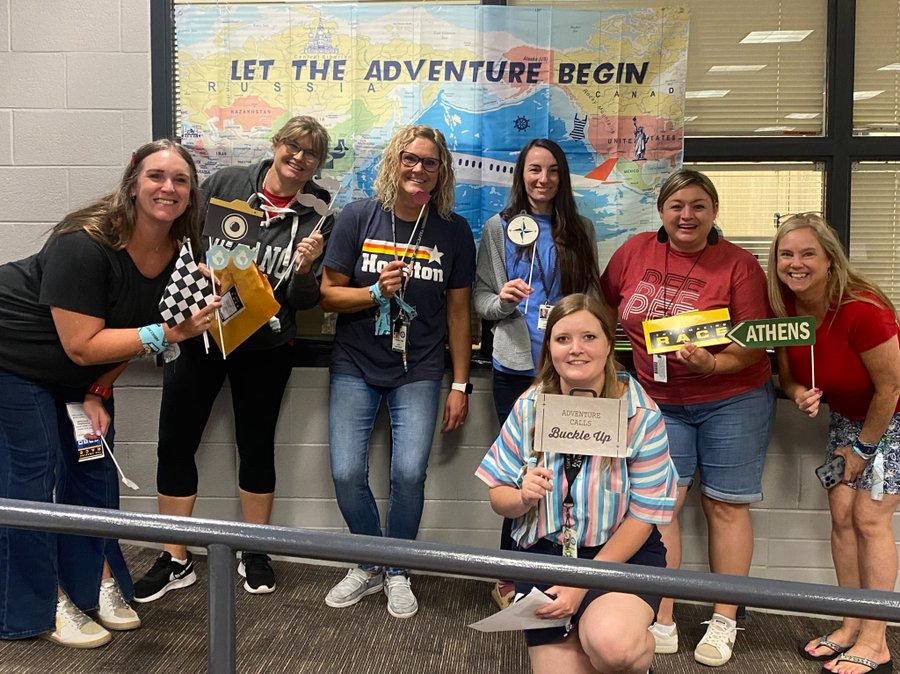 group of teachers posing in front of sign holding up prop signs