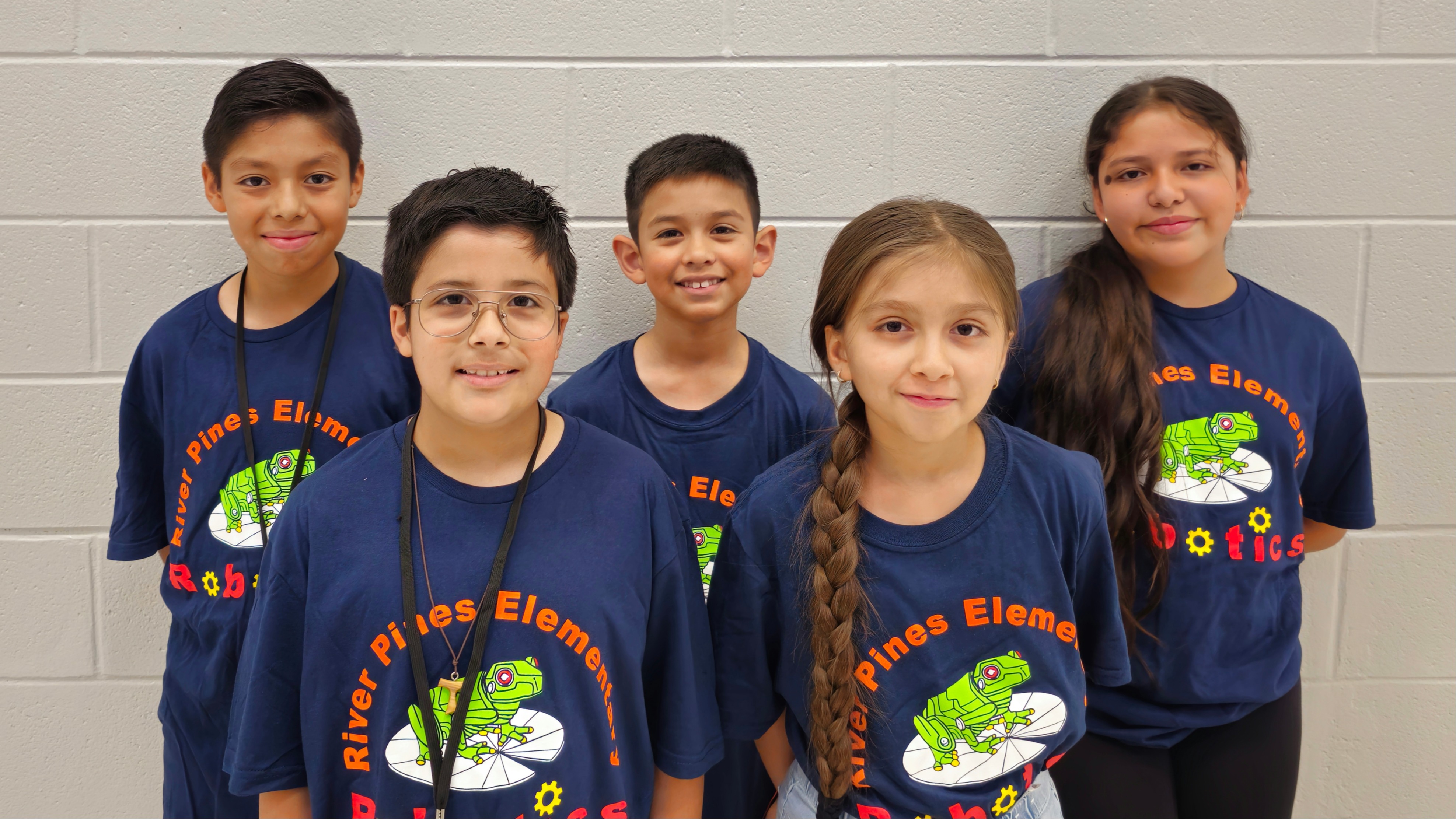 students posing in blue shirts with robotic frog