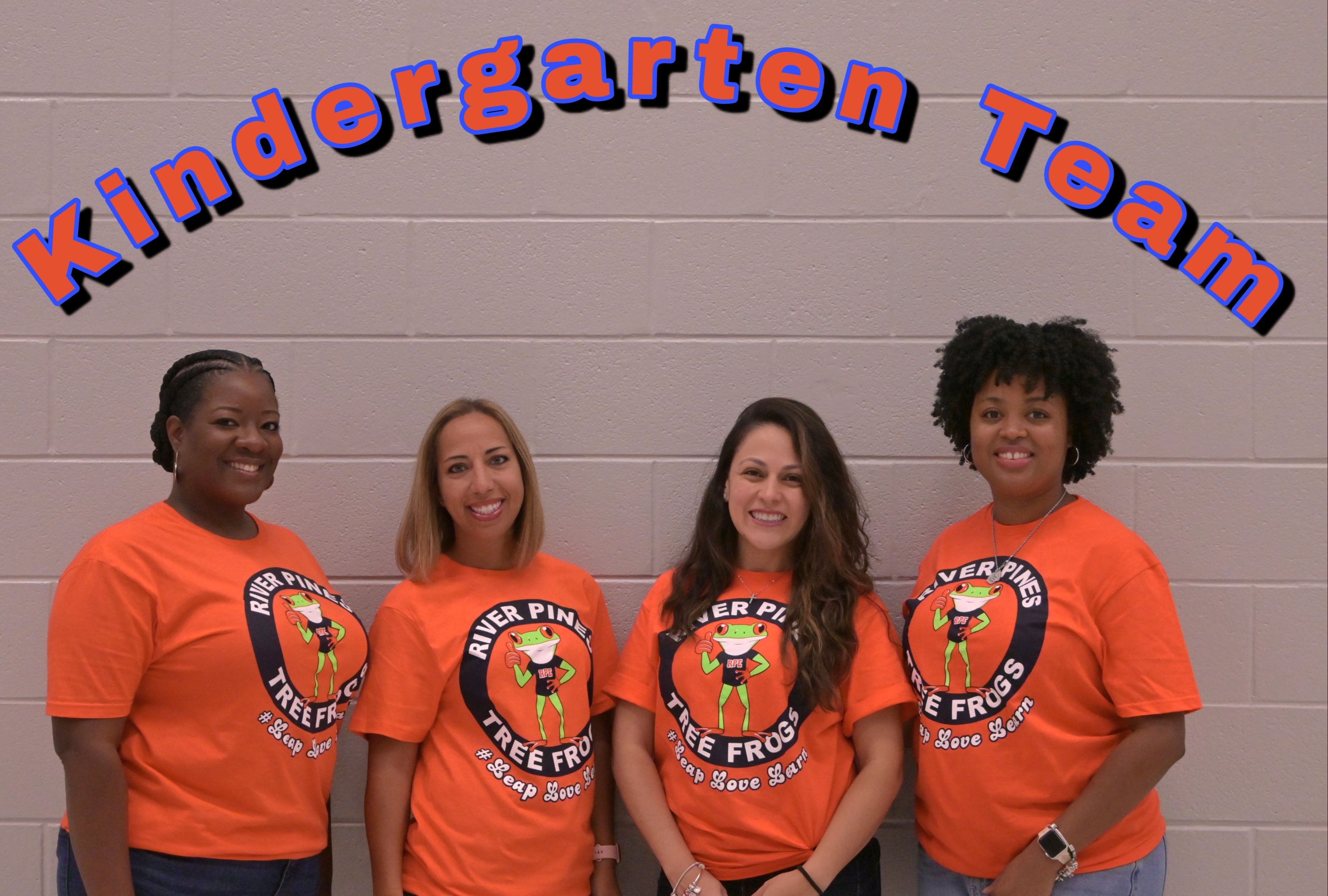 kinder team in orange shirts standing posing in front of gray brick wall