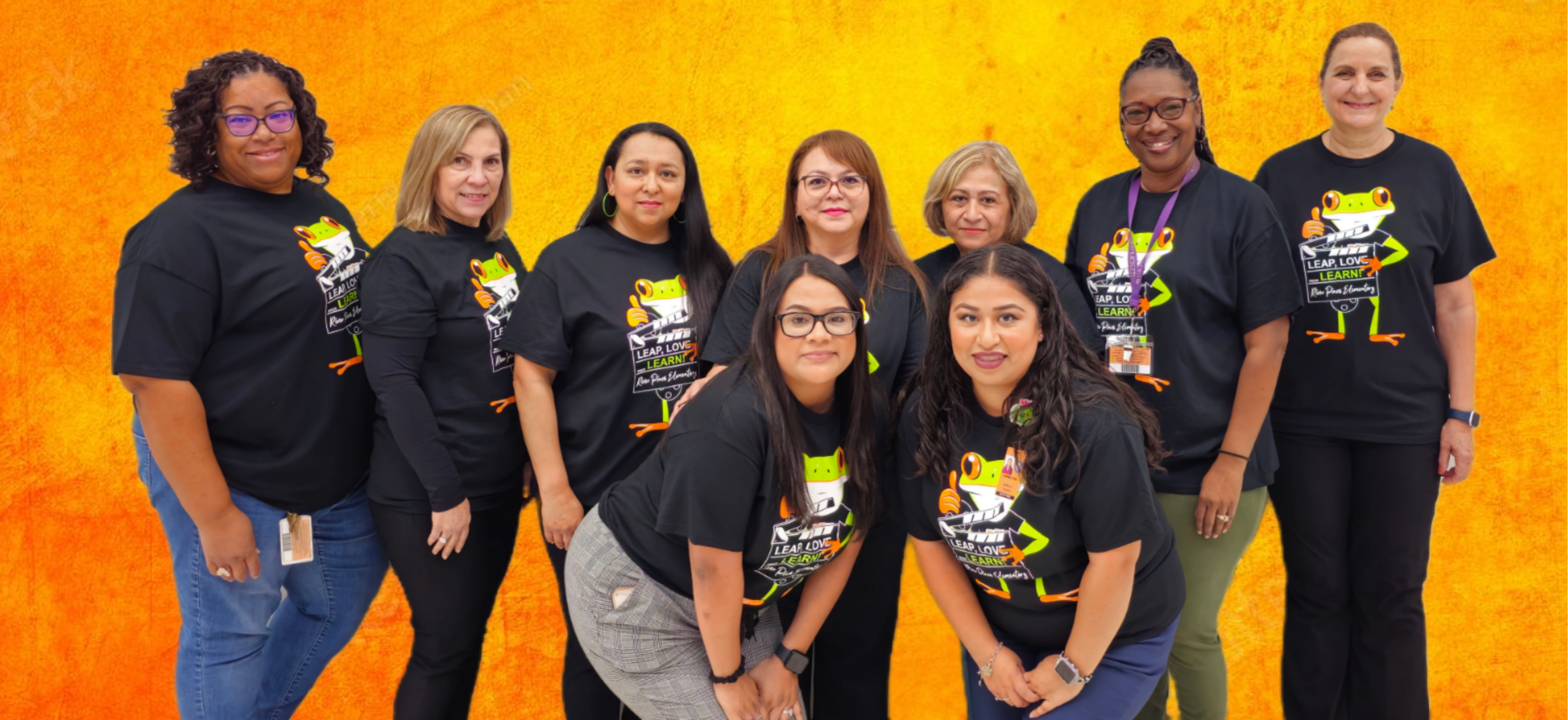 group of teachers in orange shirts posing in front of brick wall