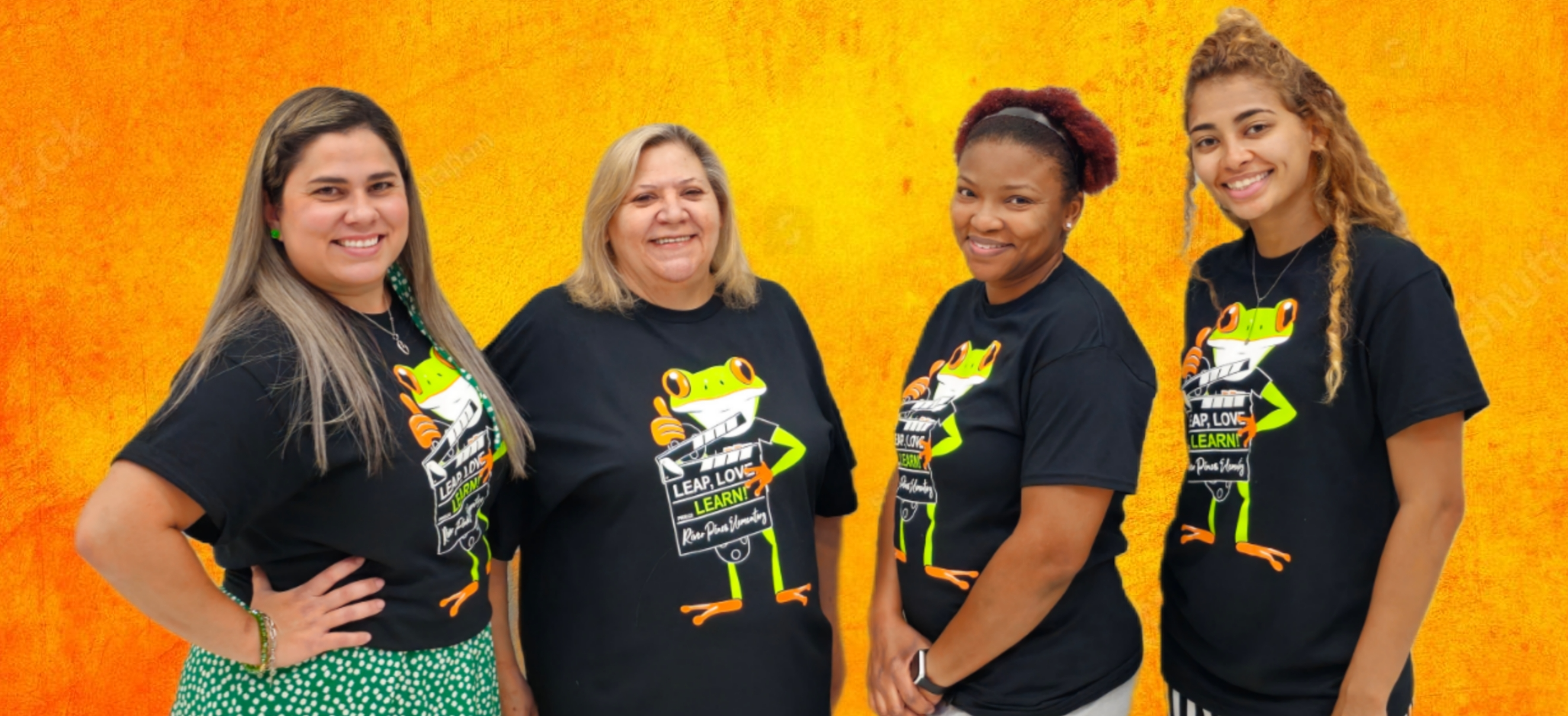 RPE 1st Grade teachers in orange shirts standing posing in front of gray brick wall