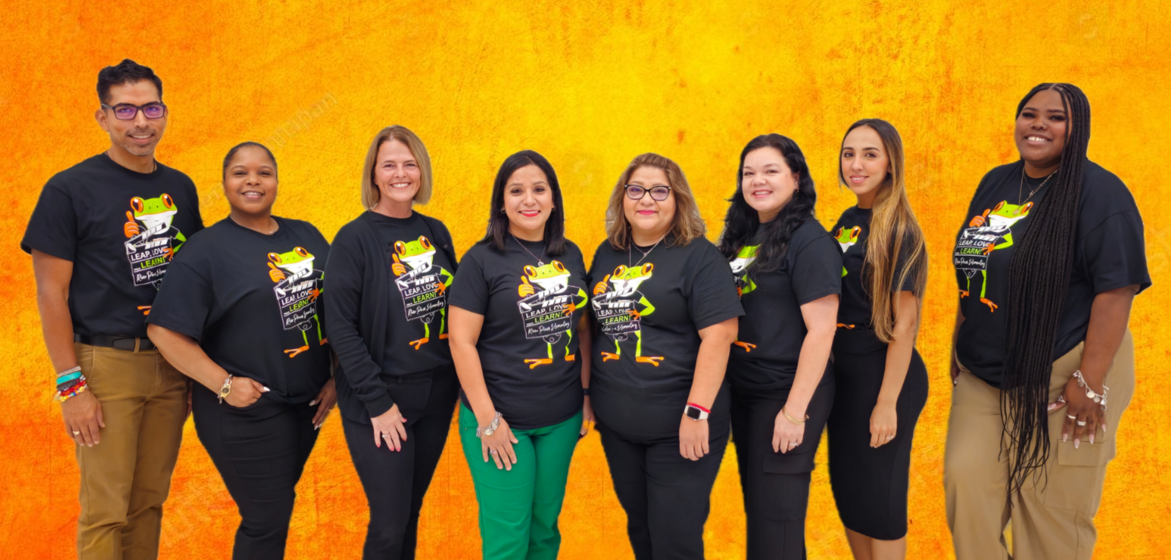 group of teachers in orange shirts standing posing in front of gray brick wall