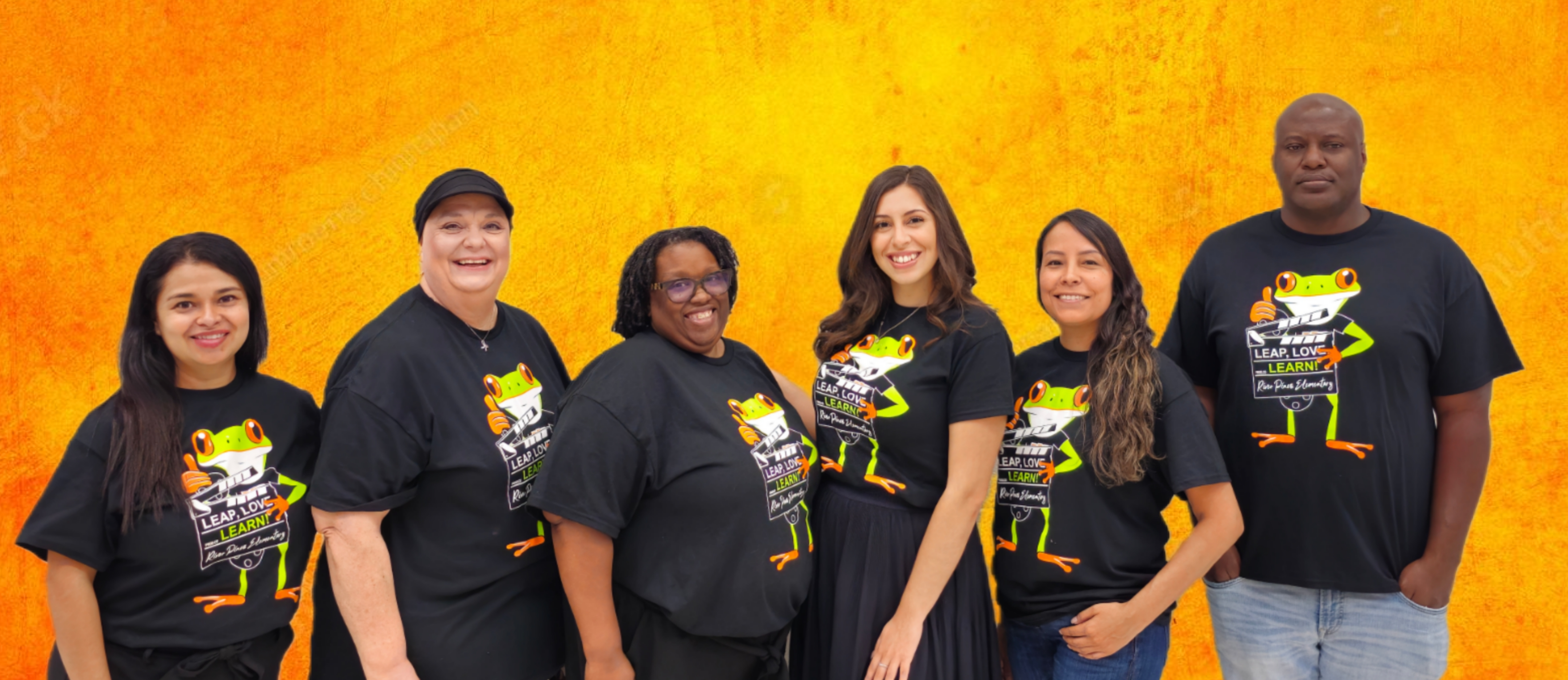 group of teachers in orange shirts standing posing in front of gray brick wall