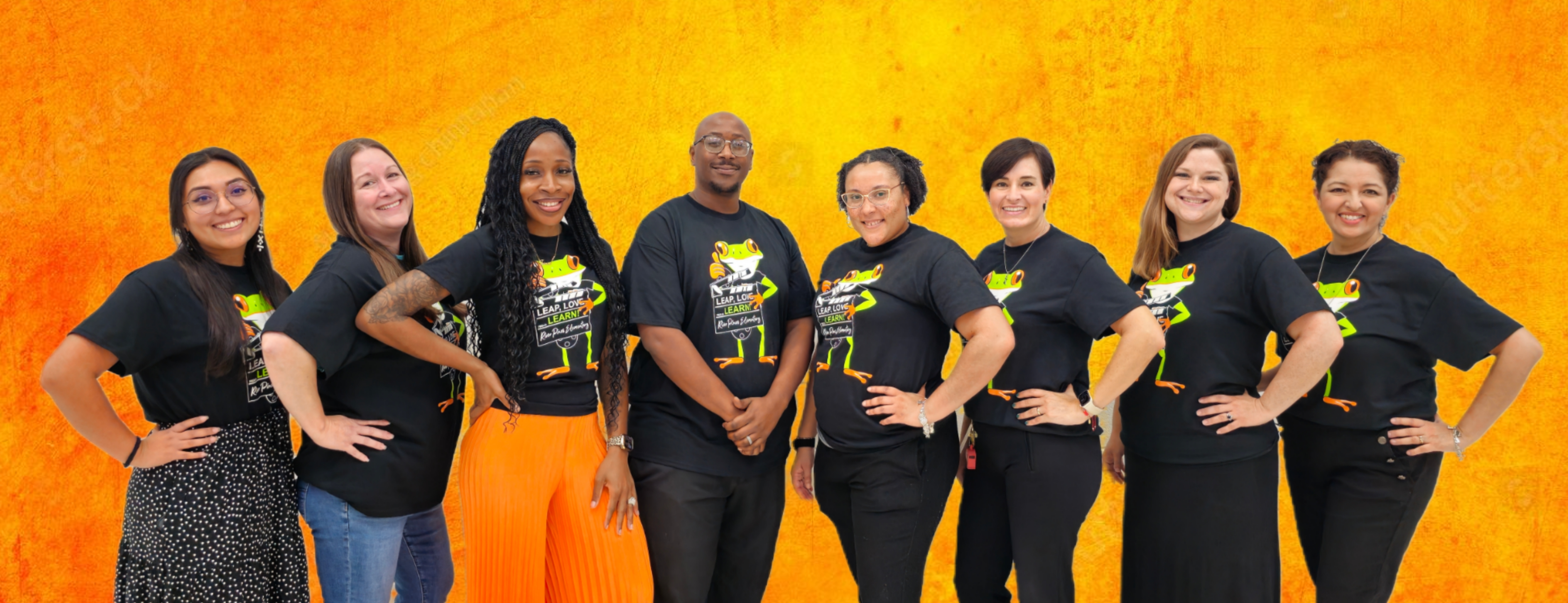 group of teachers in orange shirts standing posing in front of gray brick wall