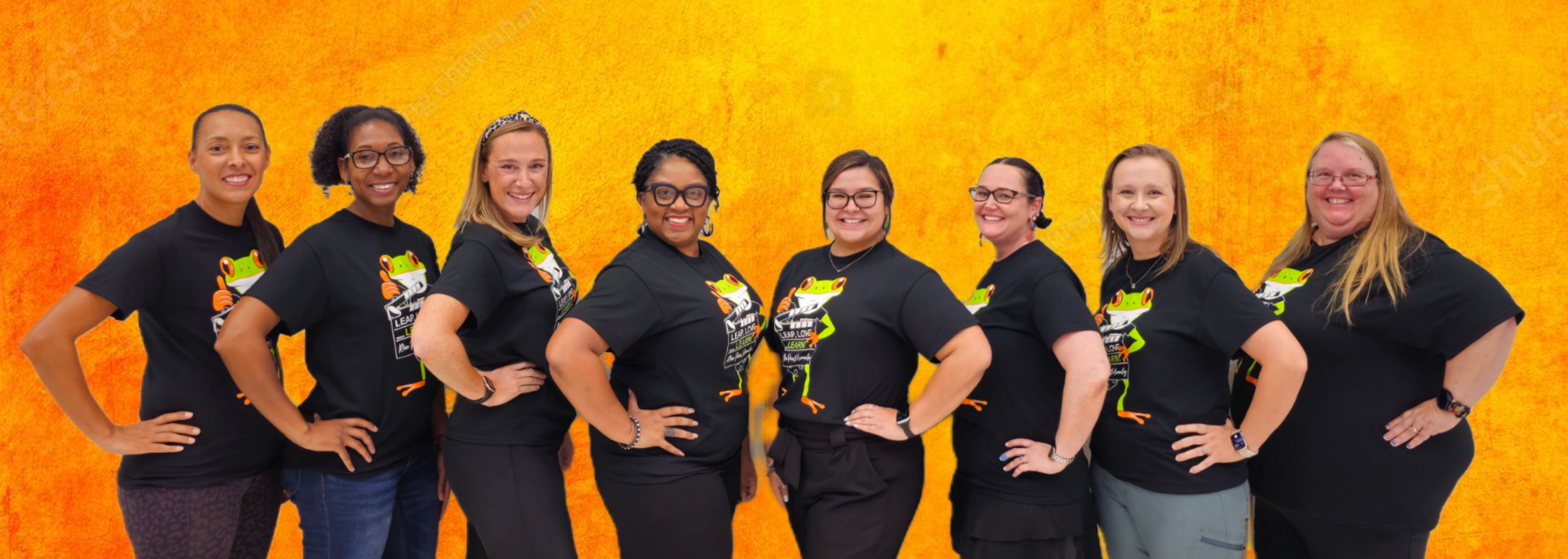 group of teachers in orange shirts standing posing in front of gray brick wall