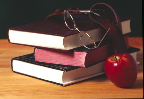 stack of books on desk with glasses and apple