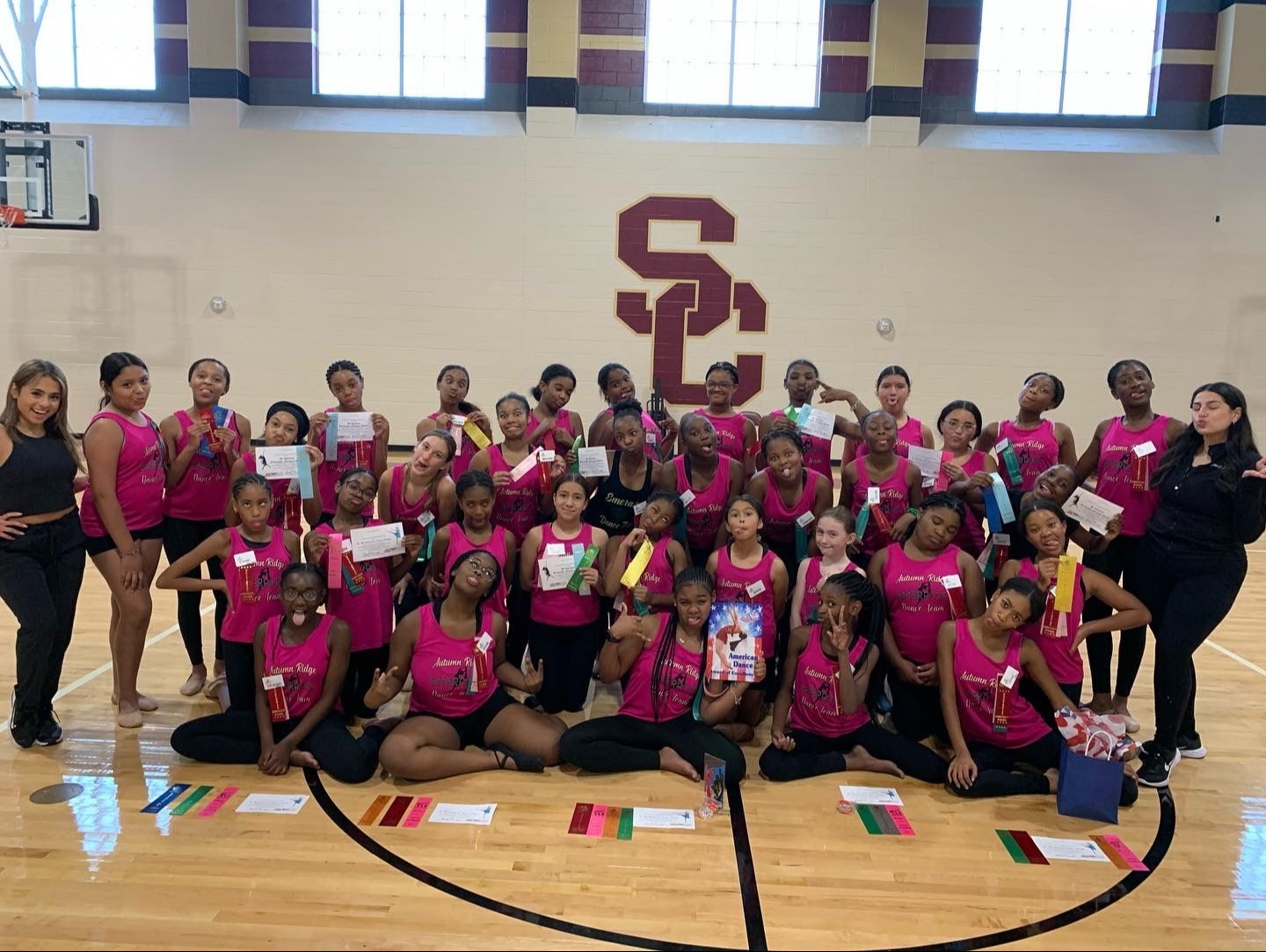 group of students in pink tank tops posing in gym