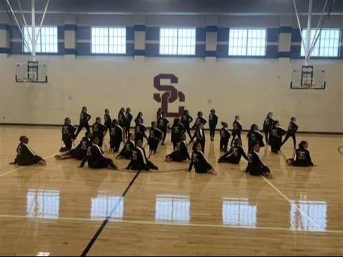 group of students in black jackets posing in dance formation in gym
