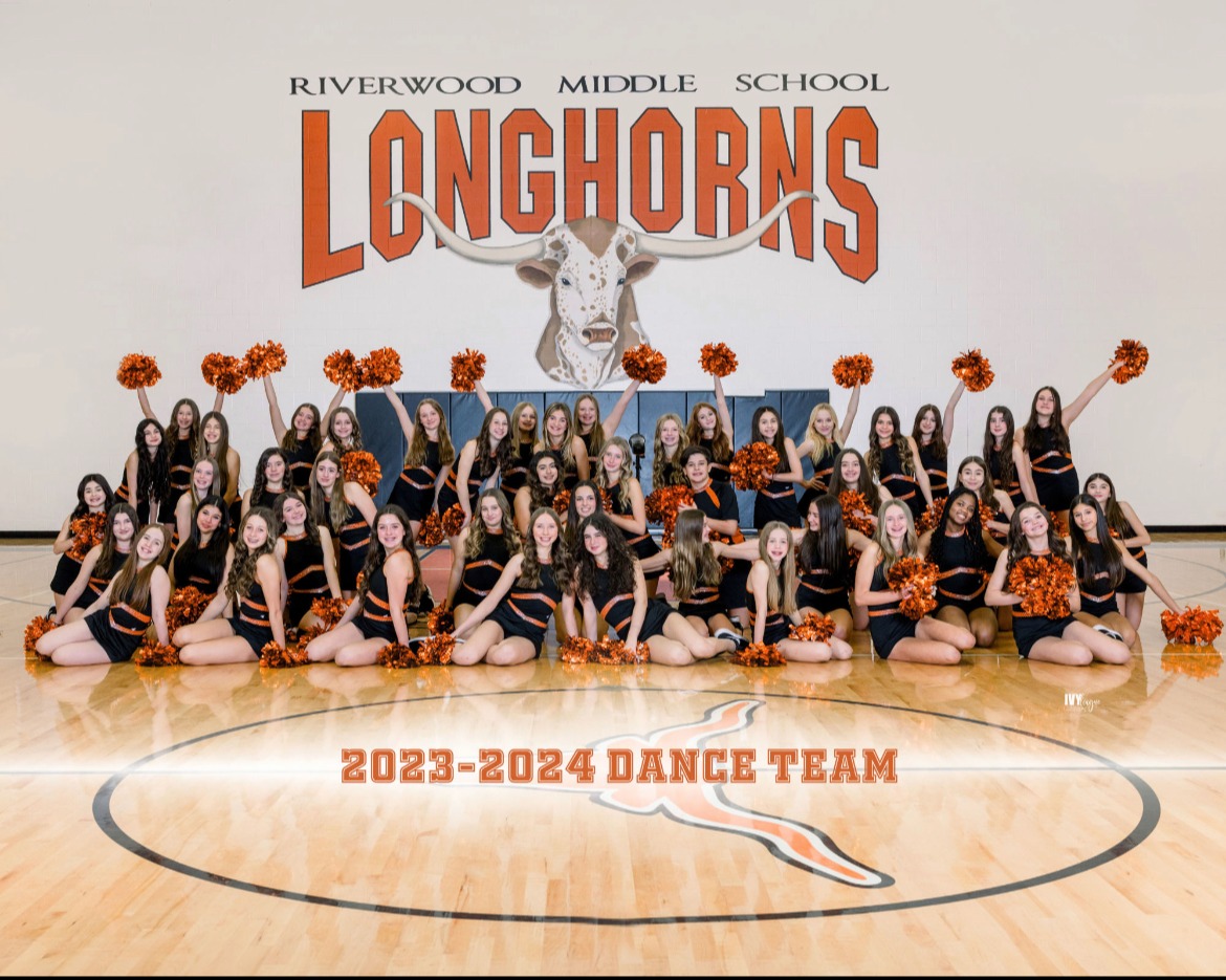dance team in black and orange uniforms with orange pom poms posing in gym with school name in background