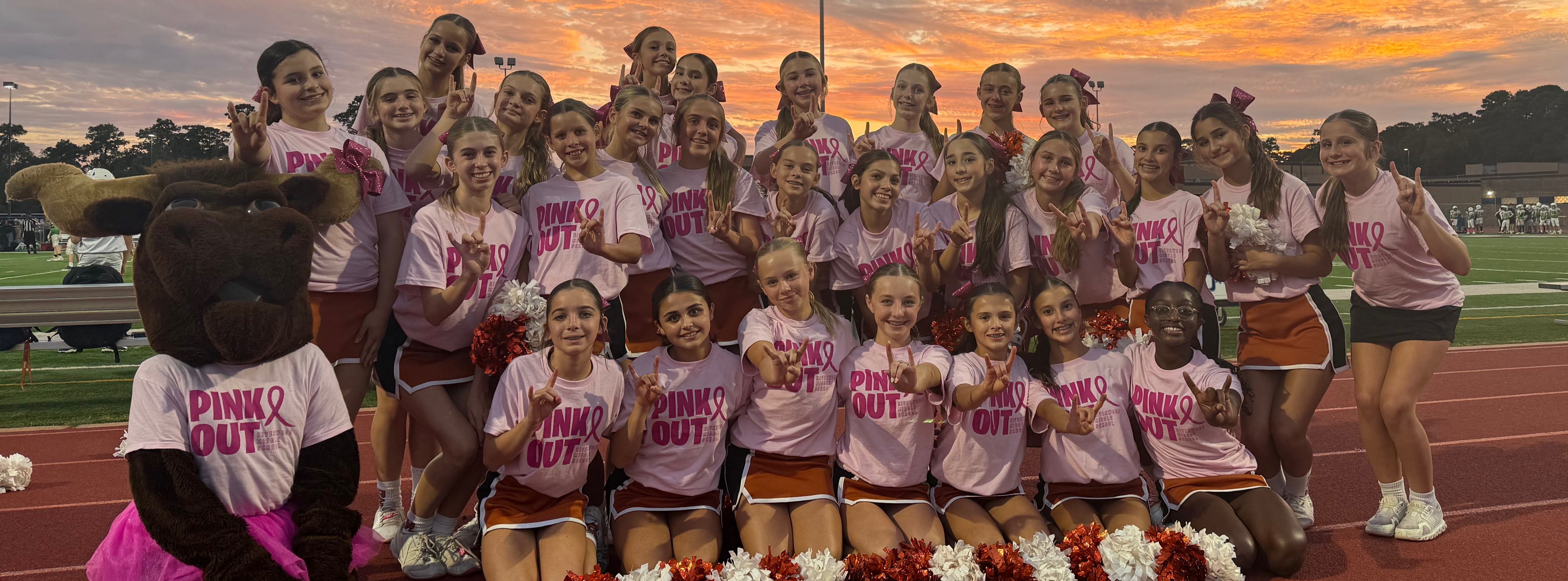 Group of girls in pink and white uniforms, posing with pom-poms on a track field.