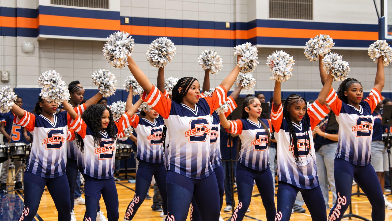 Cheerleaders in blue and white uniforms perform on a basketball court with silver pom-poms.