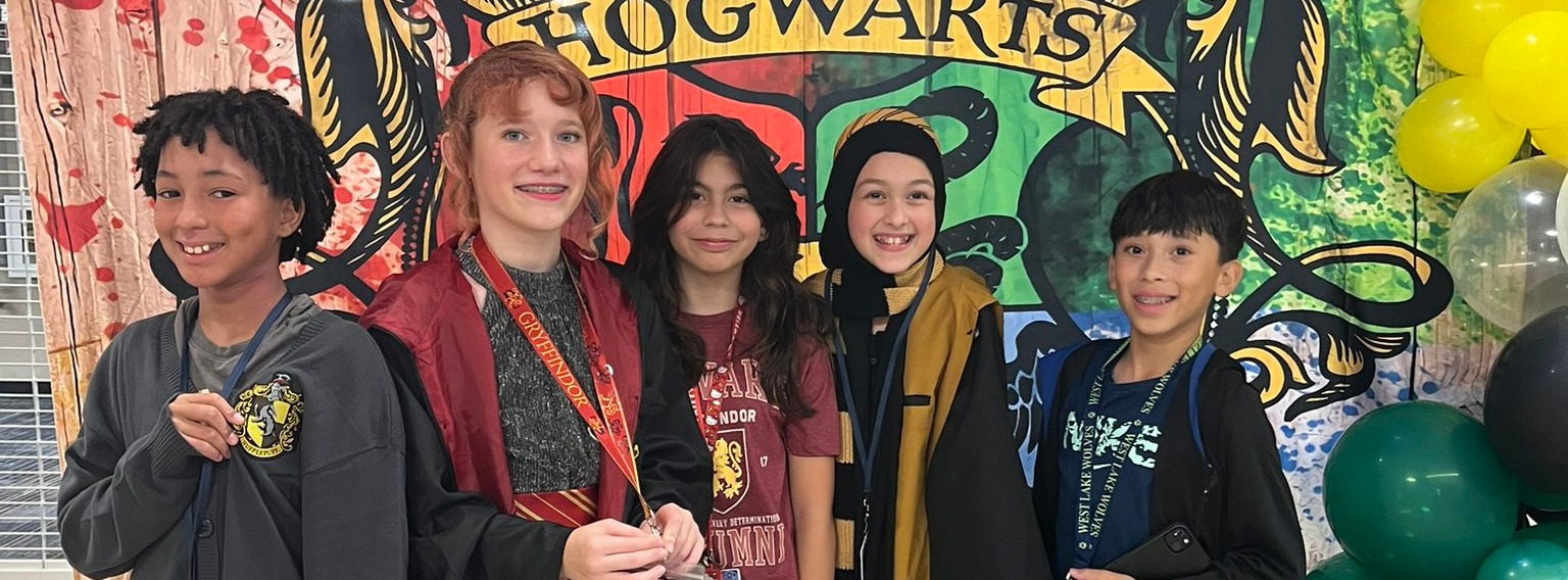 Students dressed up as Harry Potter characters stading in front of a banner that says Hogwarts