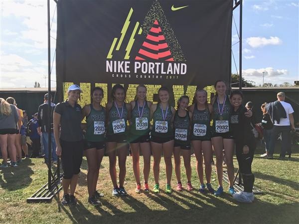 group of students with coach in green tank tops with runners bibs wearing medals standing posing outdoors