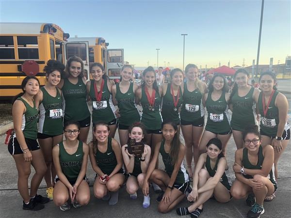 group of cross country students posing outside near buses in green tank tops