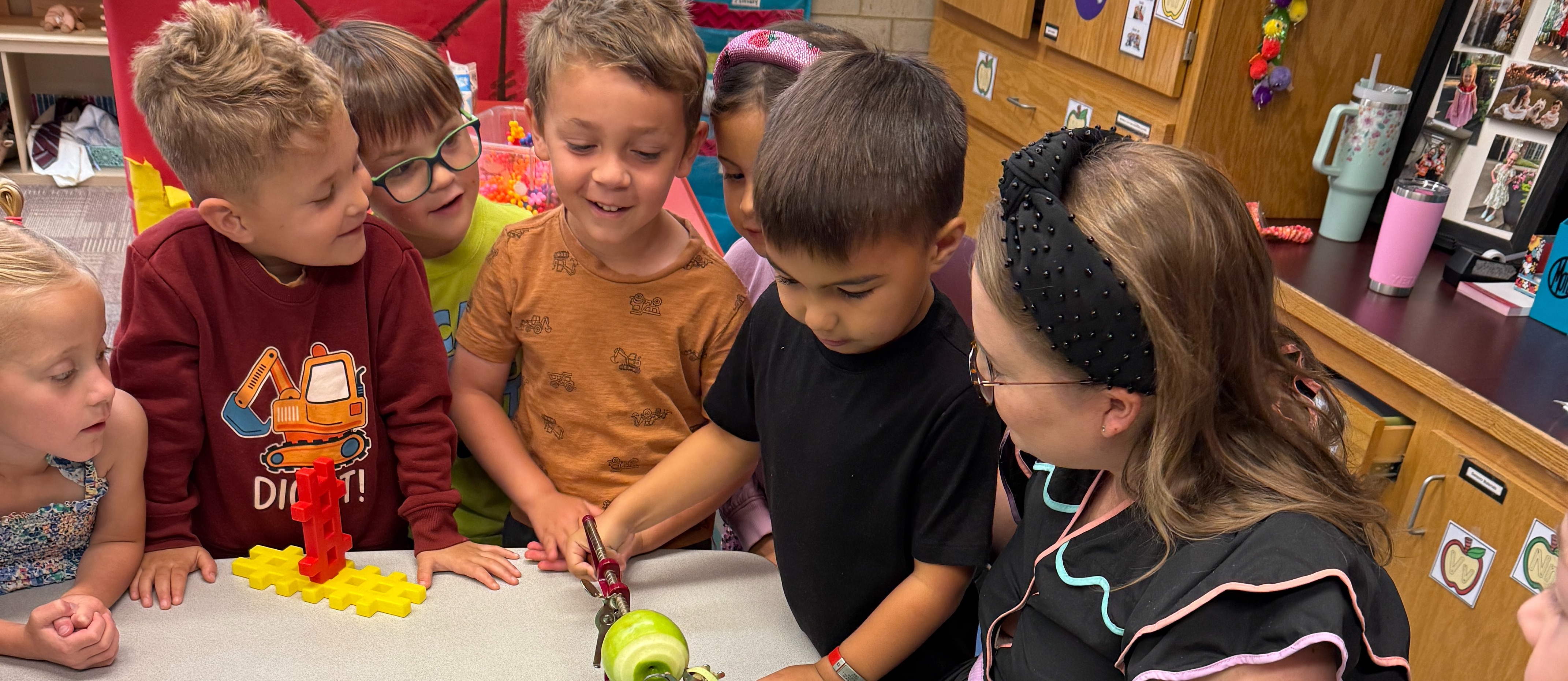 Four students gathered around a table with their teacher using an apple peeling machine