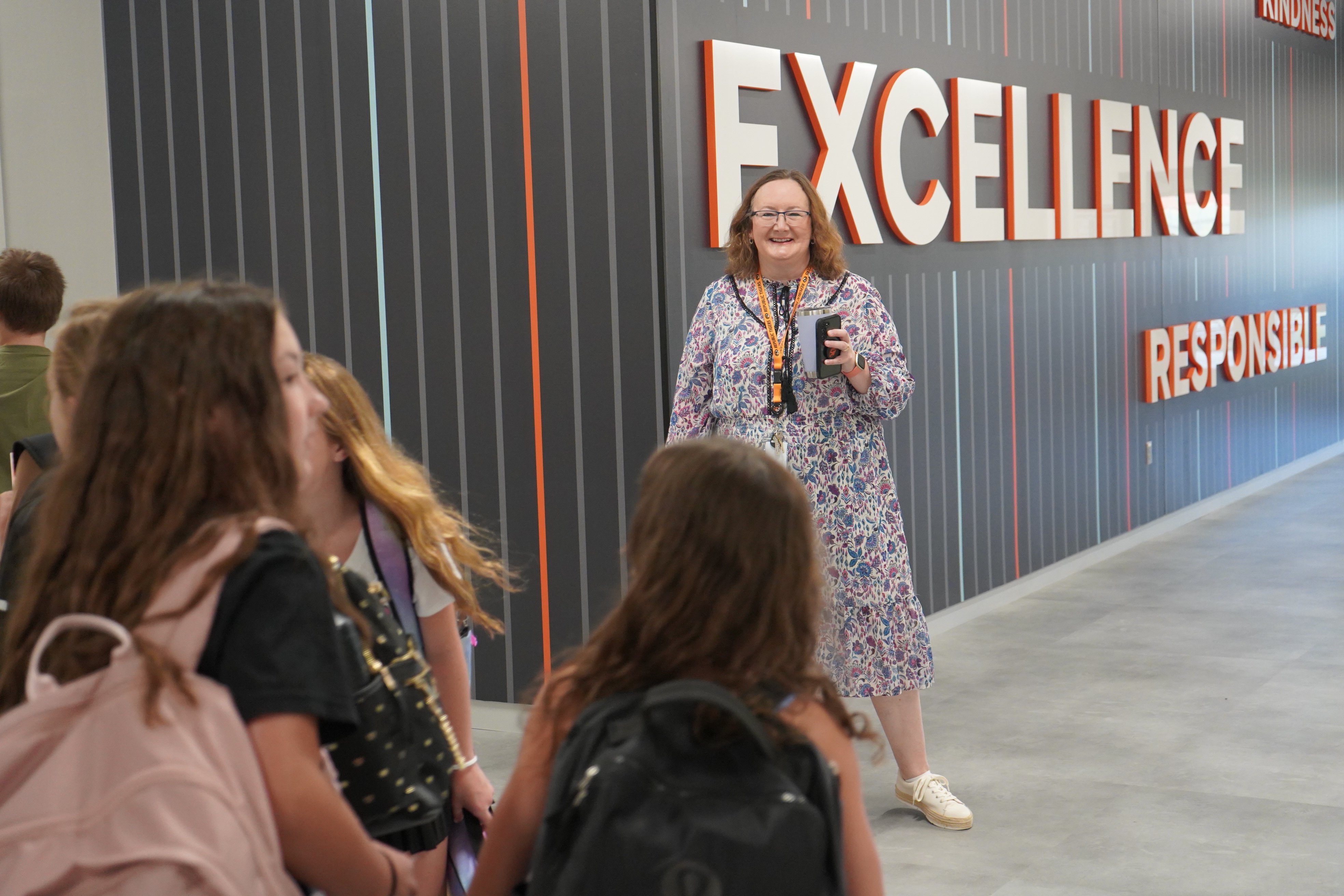 Staff member holding a coffee cup and smiling as students walk in