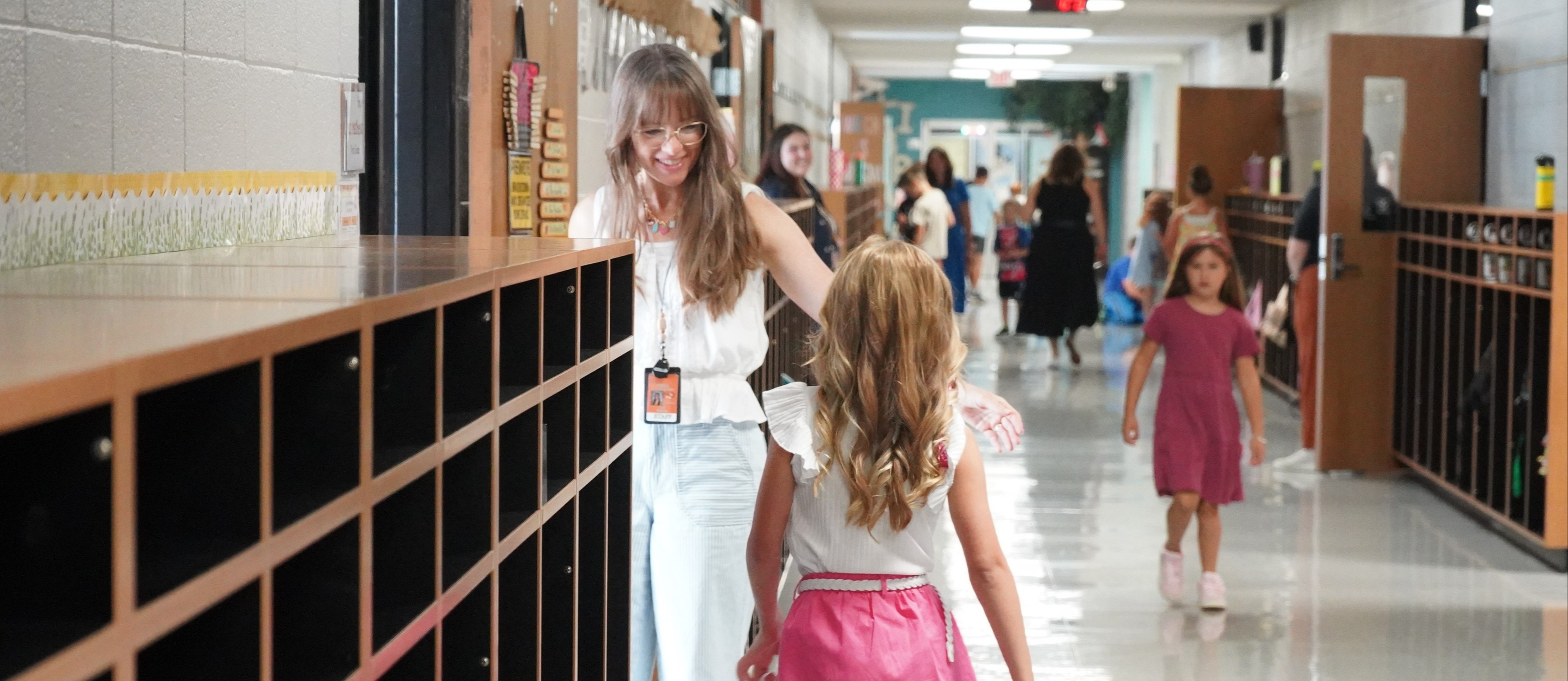 Student walking down the hallway, teacher welcoming her into the classroom