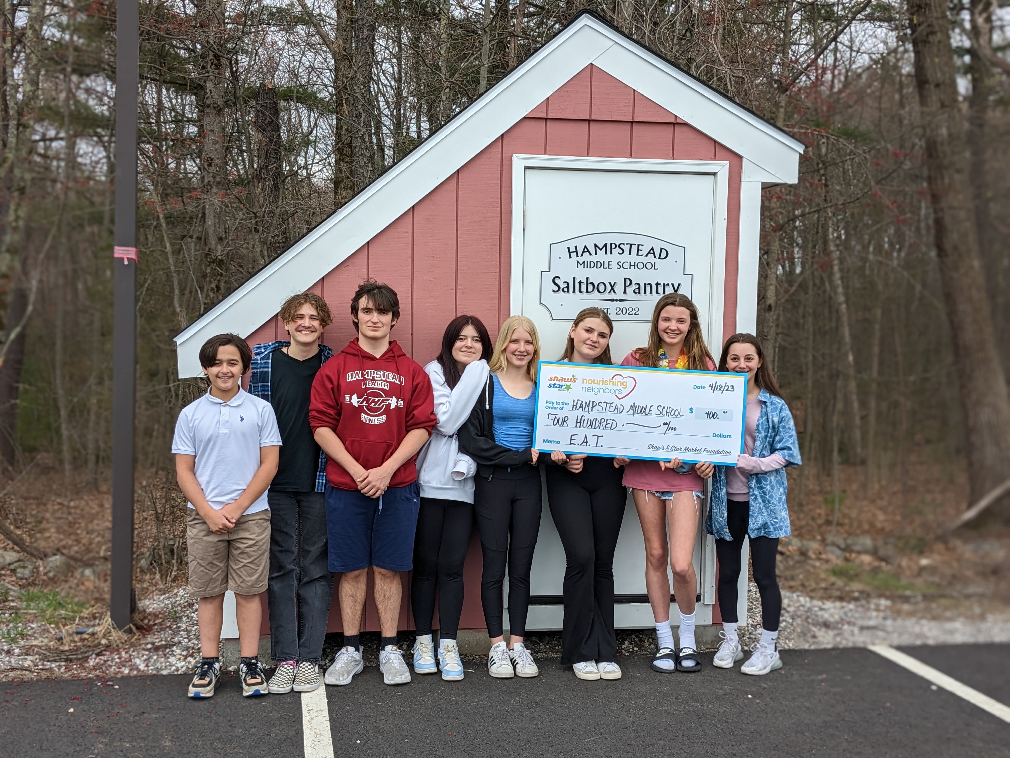 Hampstead Middle School students standing in front of the Saltbox Pantry food pantry they had worked on. They are holding a large check from Shaw's donating money to the school.