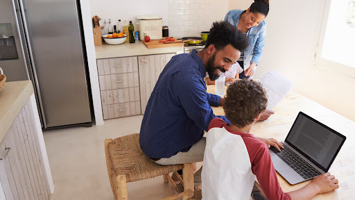 family sitting down at a table using a laptop