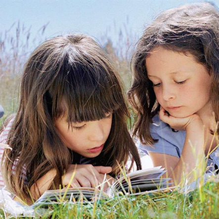 Two girls reading a book out in tall grass