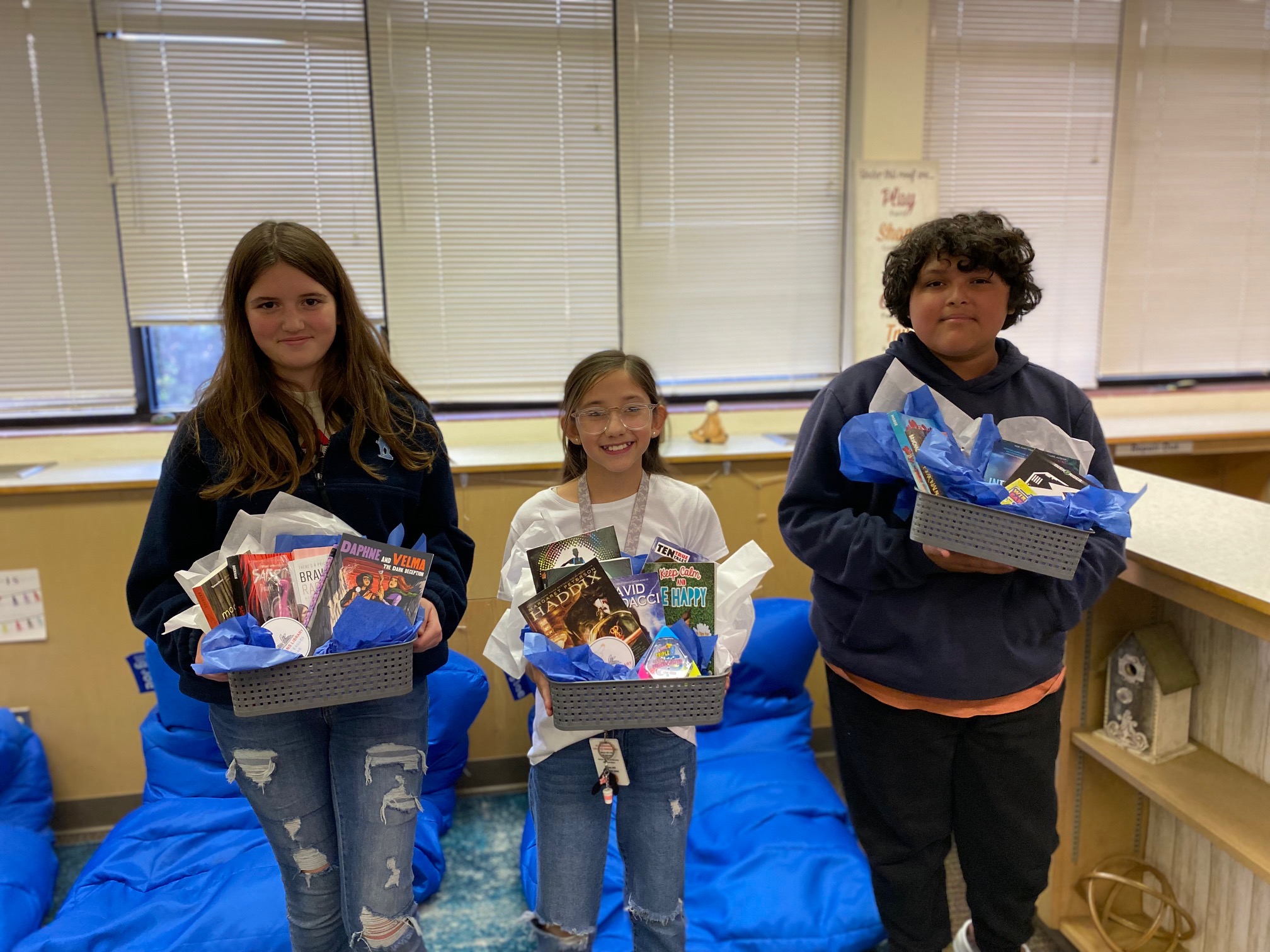 Three students holding prize buckets filled with books