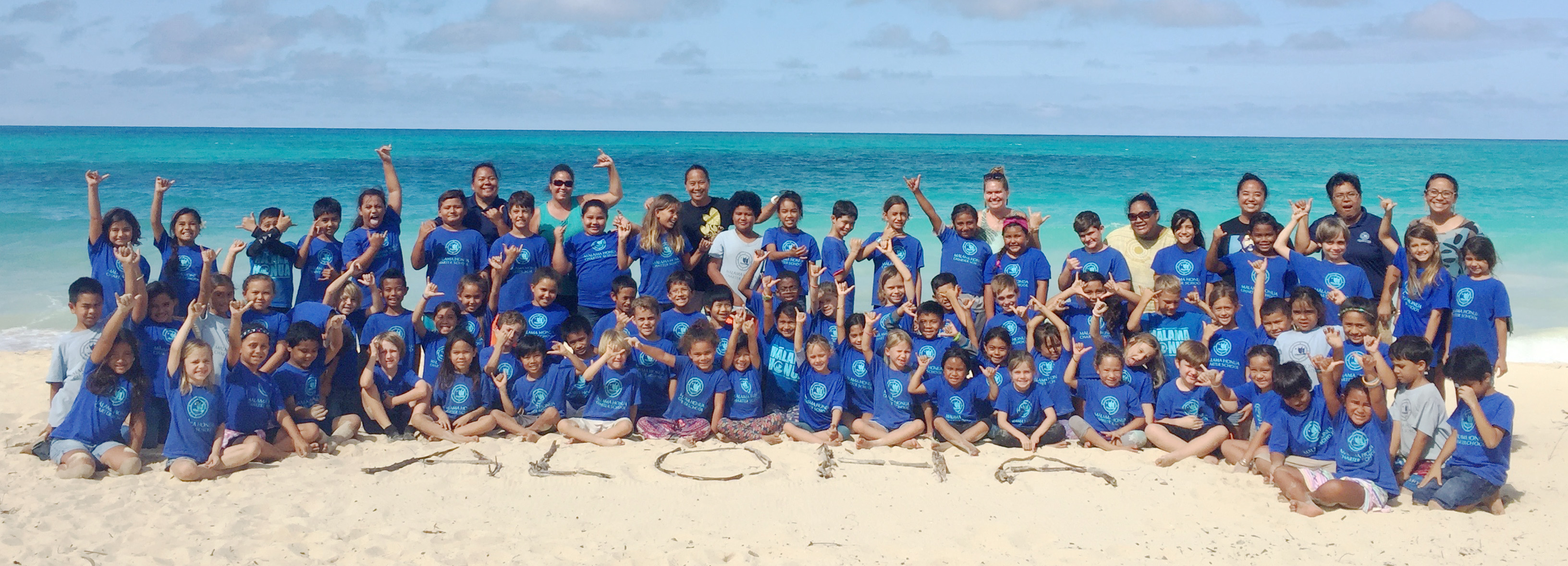 group photo of students on beach with aloha written in sand