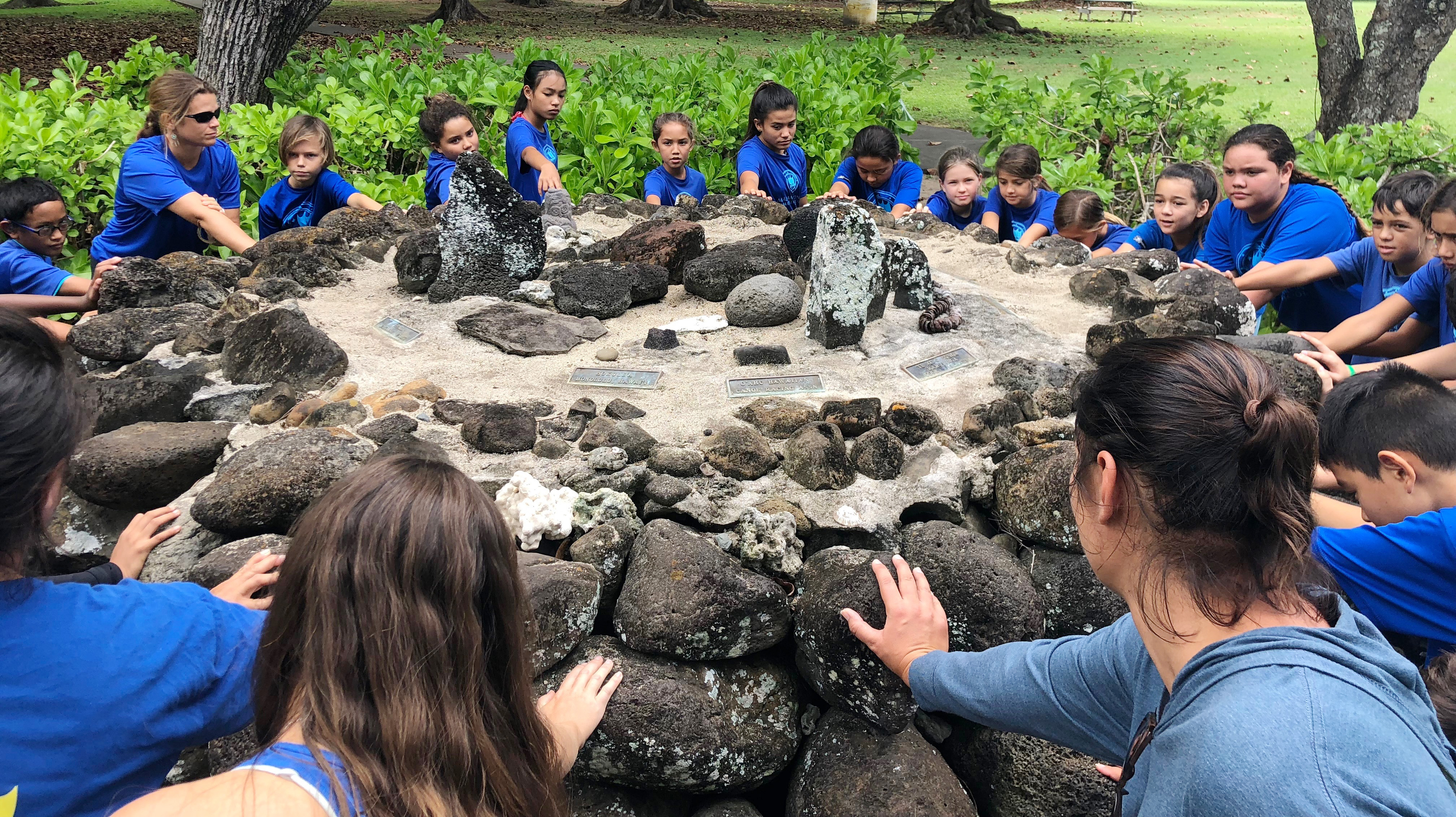 group of students in a circle putting hands on rocks