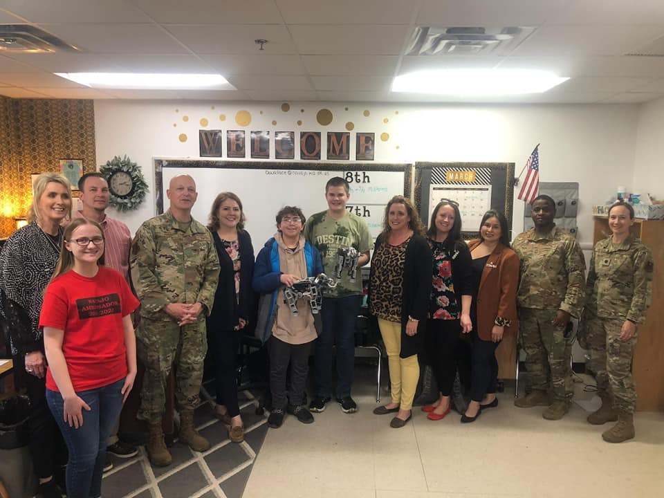 military personnel pose with STEM students with their robots