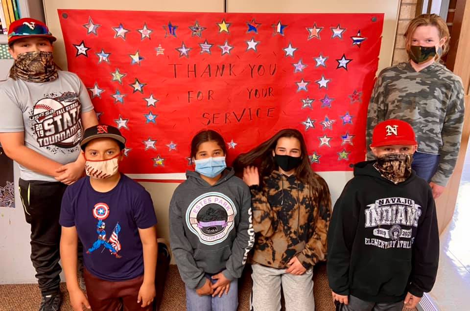 Students dressed in red/white/blue in front of sign reading "Thank you for your service"