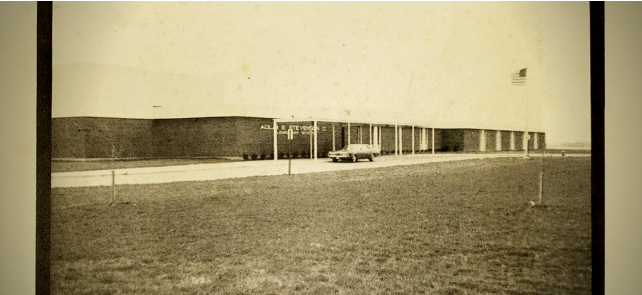Black and white photo of campus with an old car in front of the school building