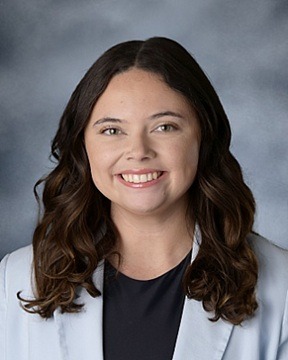 Female smiling with dark hair and light blue jacket over black shirt.