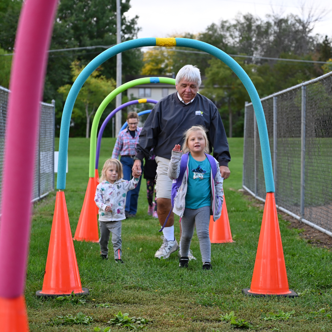 Caregiving and students walking through pool noodle cone arches on Walk to School Day