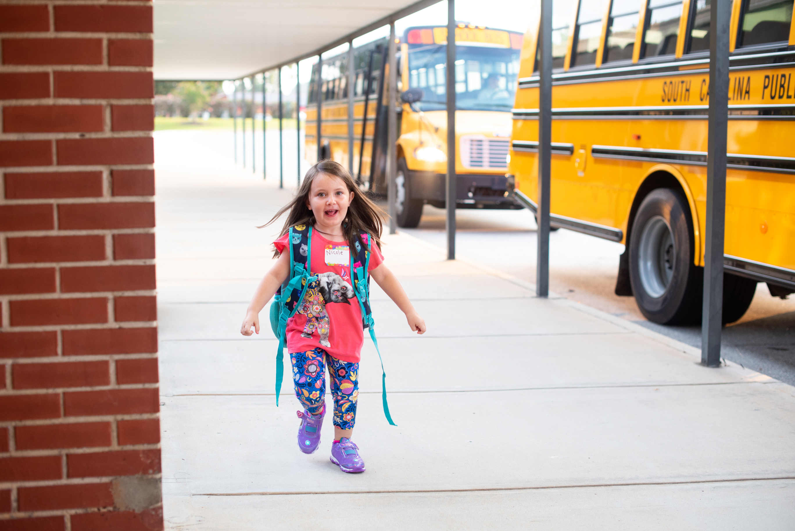 A little girl running next to a yellow school bus