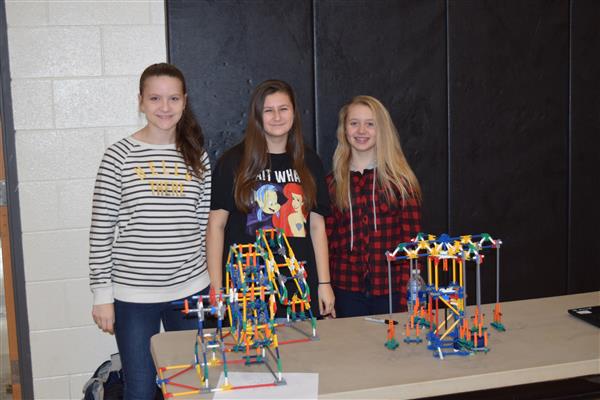 Three students standing next to their experiment and smiling at the camera