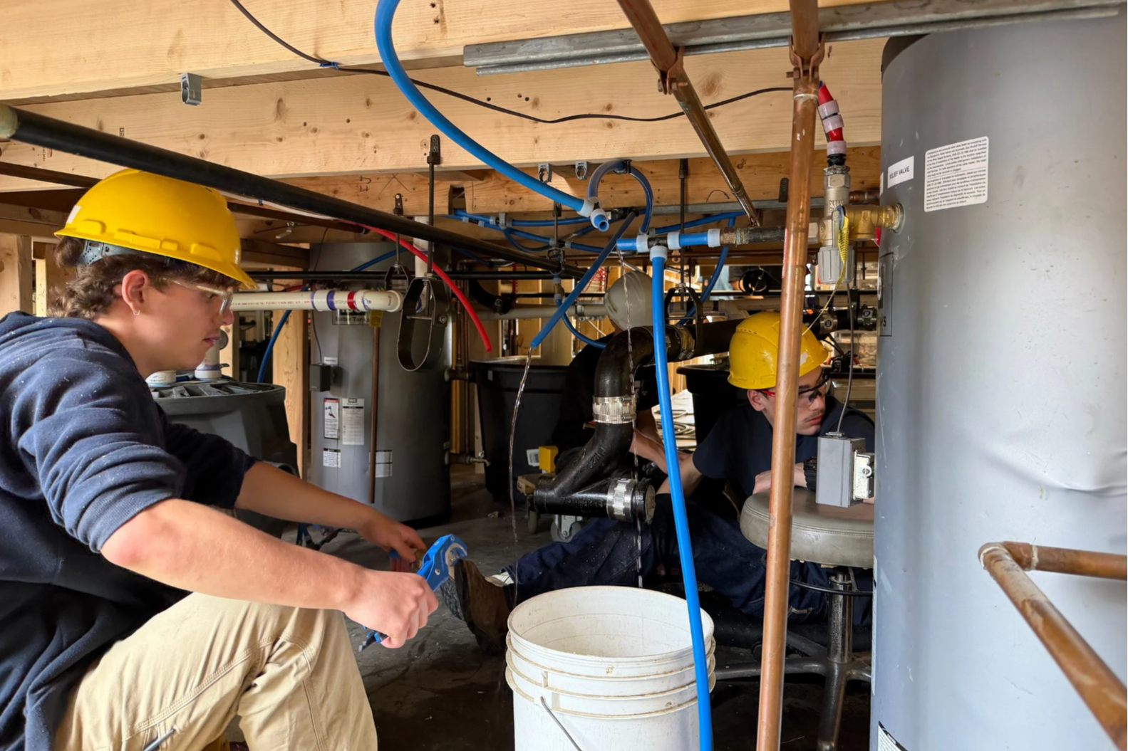 Two people wearing hard hats and blue shirts working in an area with large water tanks.