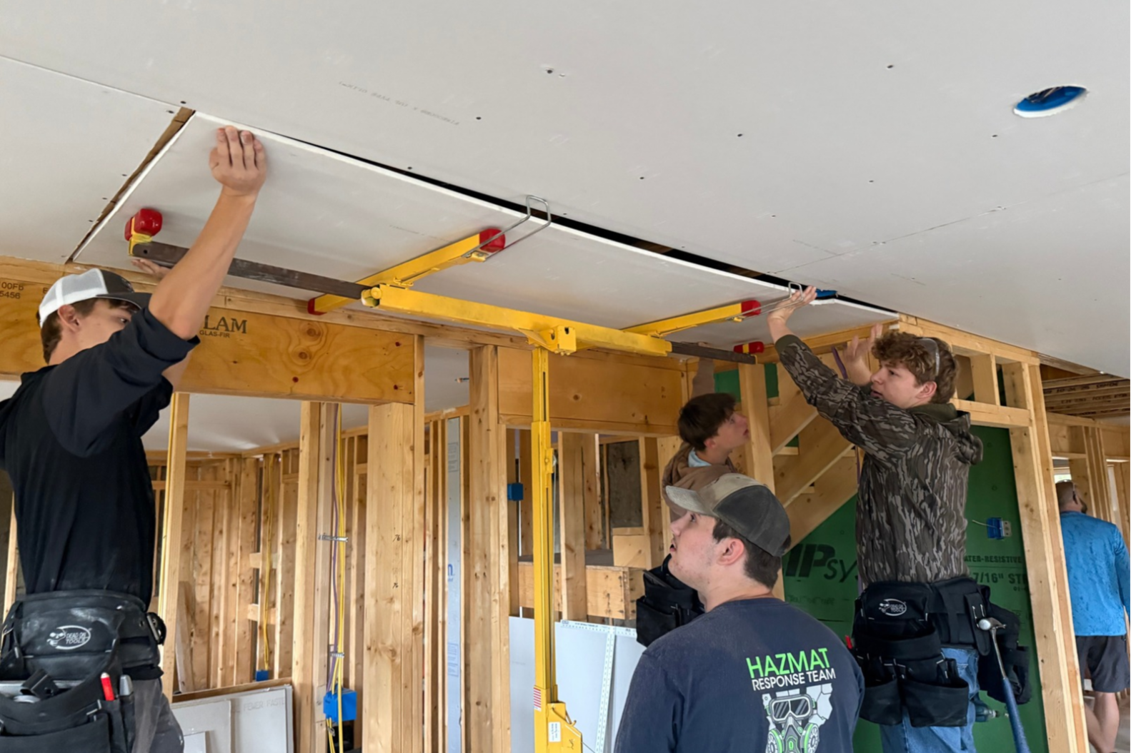 A group of people are inside a room under construction. Two are on a lift, reaching for a ceiling.